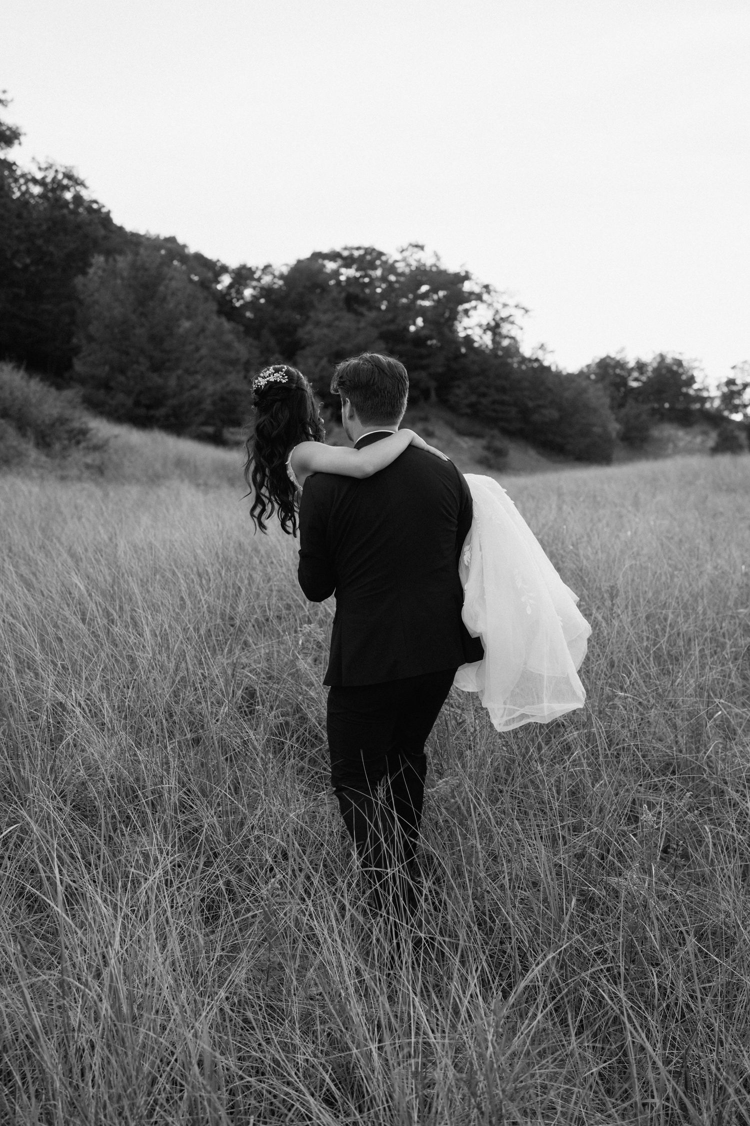 Romantic black and white photo of a couple embracing in a tall grass field.