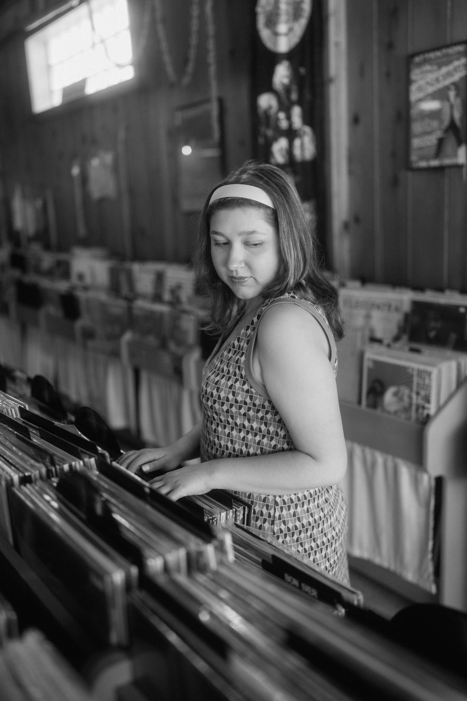 Black and white photo of someone browsing through vinyl records in a vintage shop setting.
