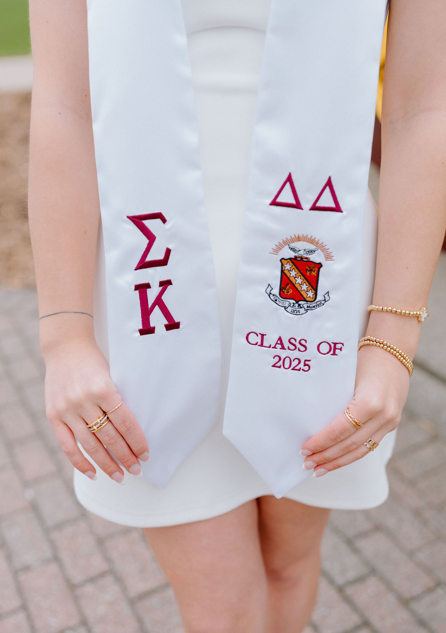 Close-up of graduation sashes showing Greek letters and Class of 2025 embroidery in red on white fabric.