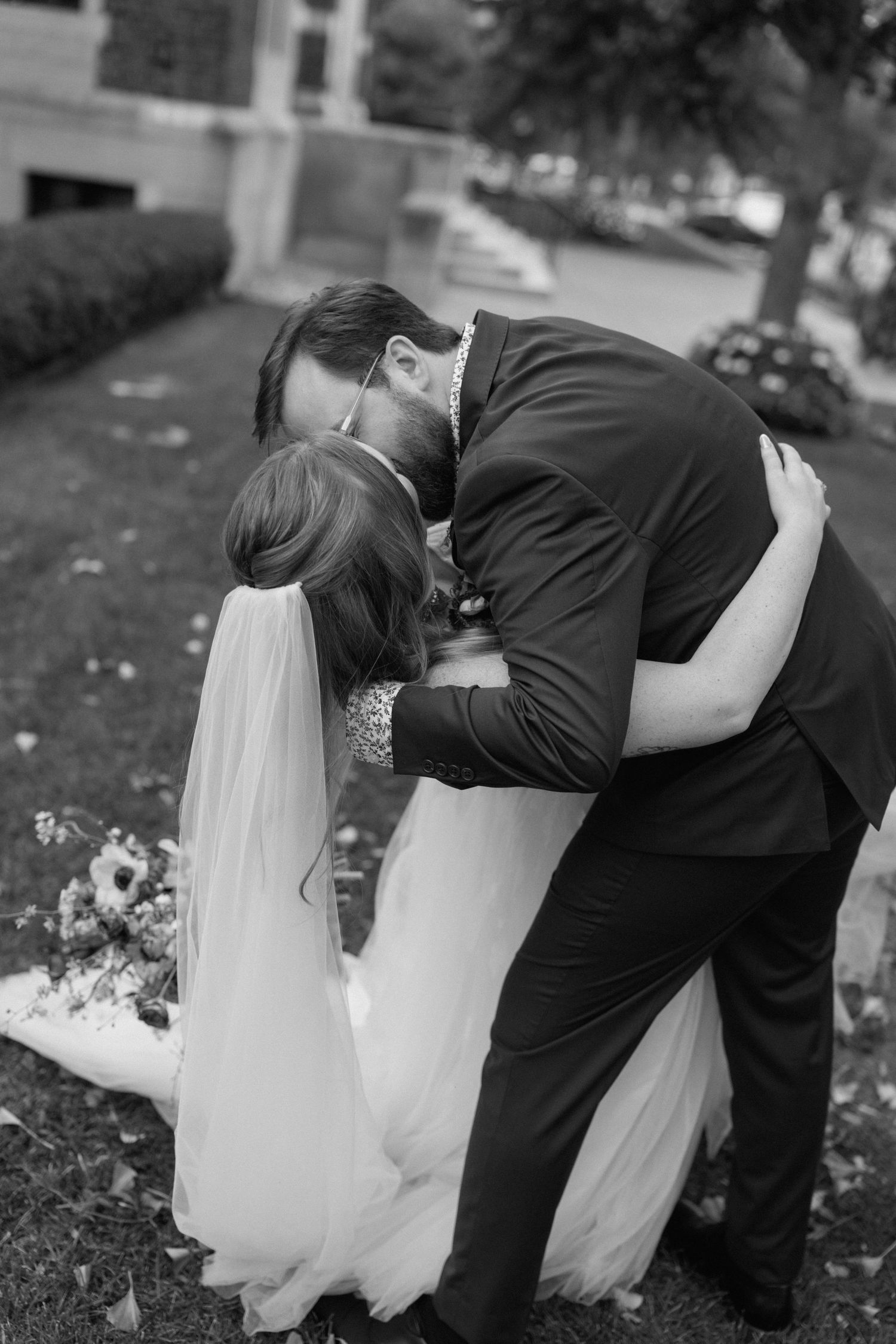 A romantic black and white wedding photo series showing a couple in a dipping kiss pose outdoors.