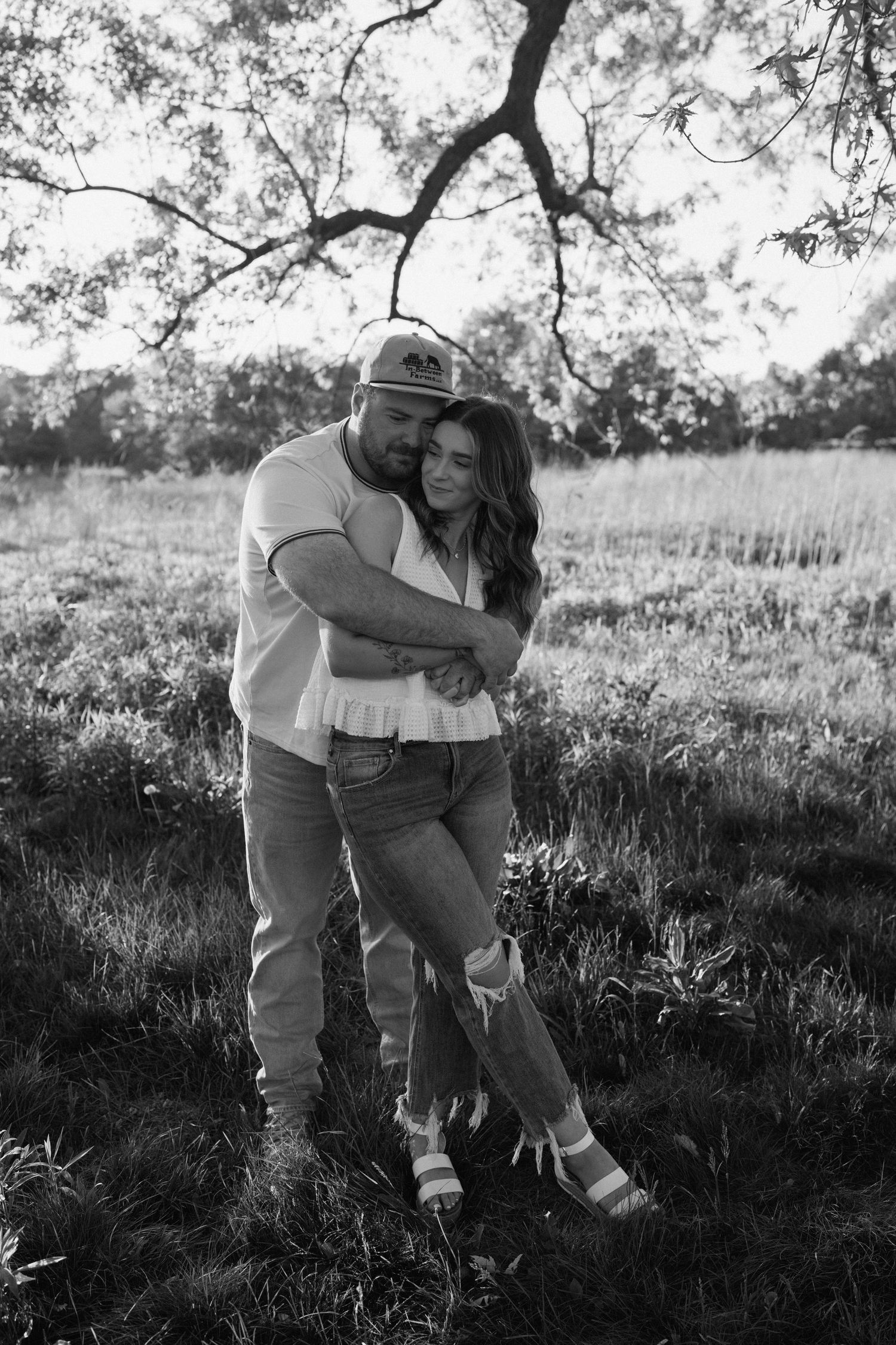 Black and white portrait of a couple playing and embracing in an outdoor field.