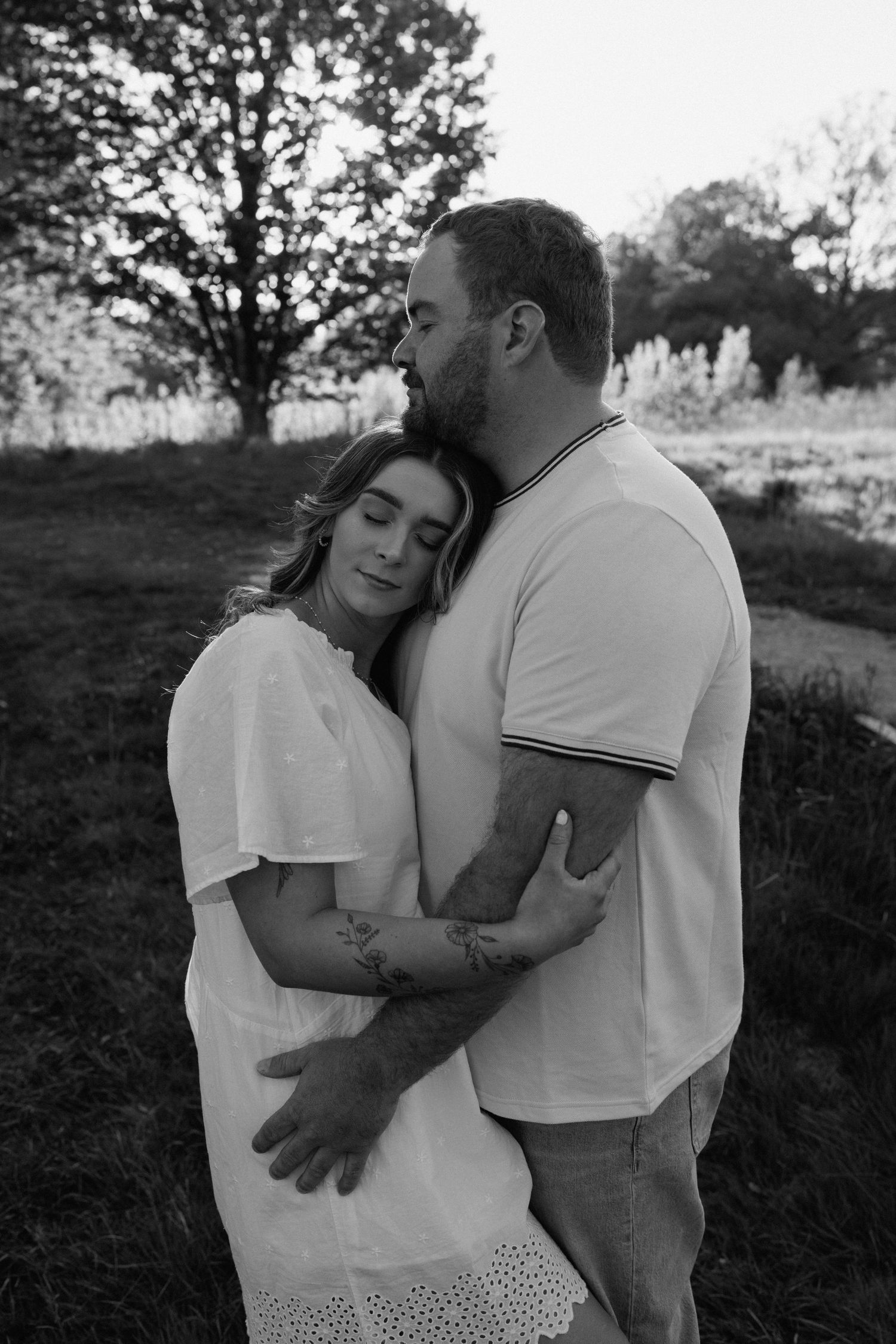 Black and white photo of a couple embracing outdoors in matching white outfits.