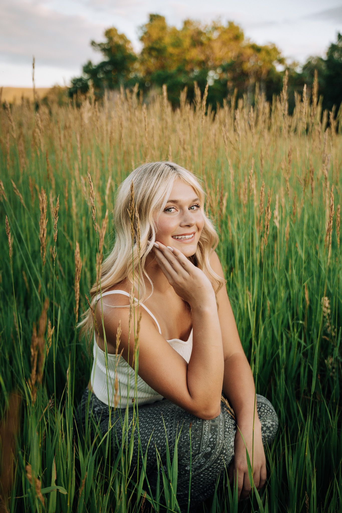 Girl crouching in a green bush holding her head with ehr hand.
