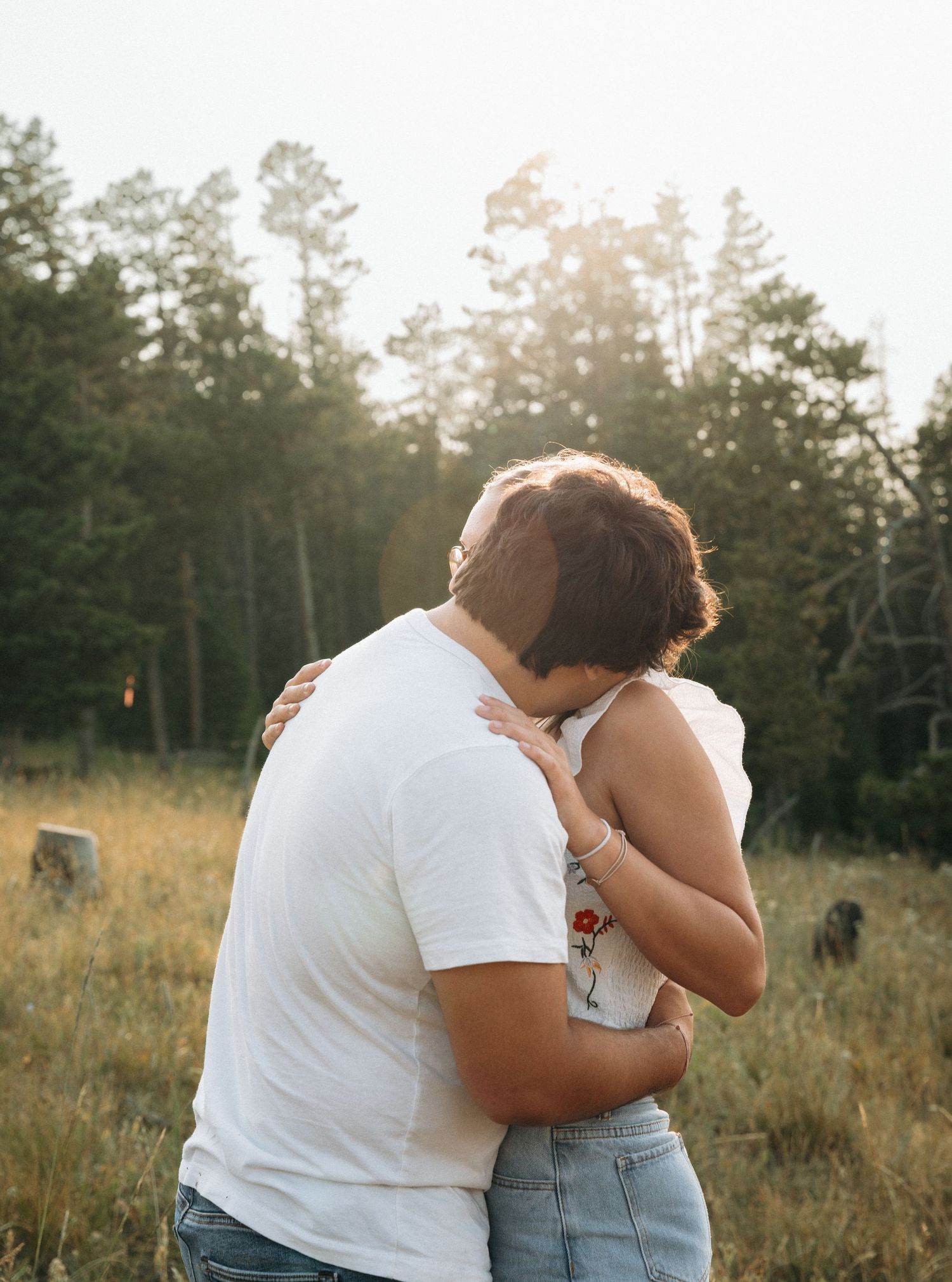 Girlfriend posing with boyfriend in field with sun in the back.