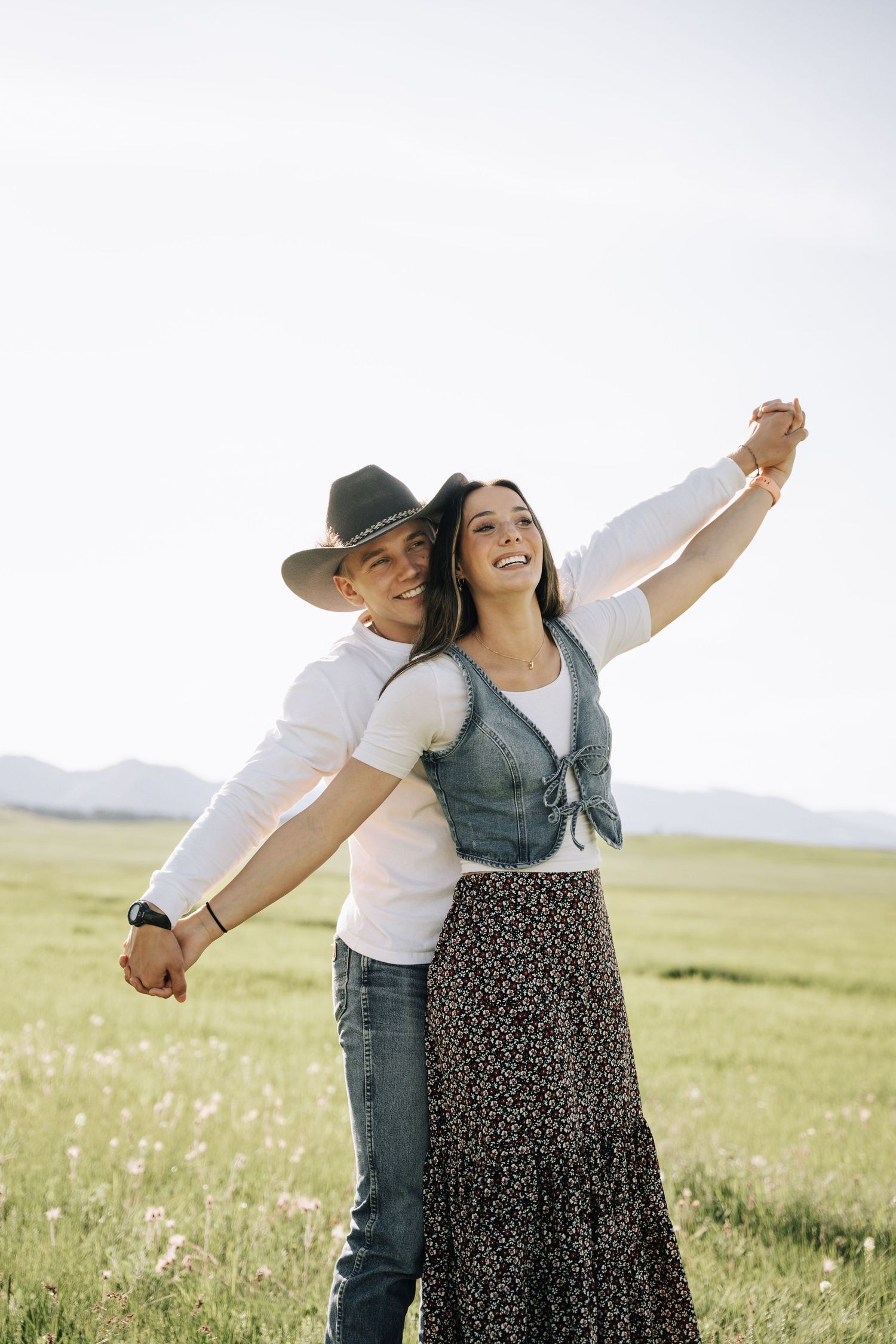Girlfriend posing with boyfriend in field with sun in the back.