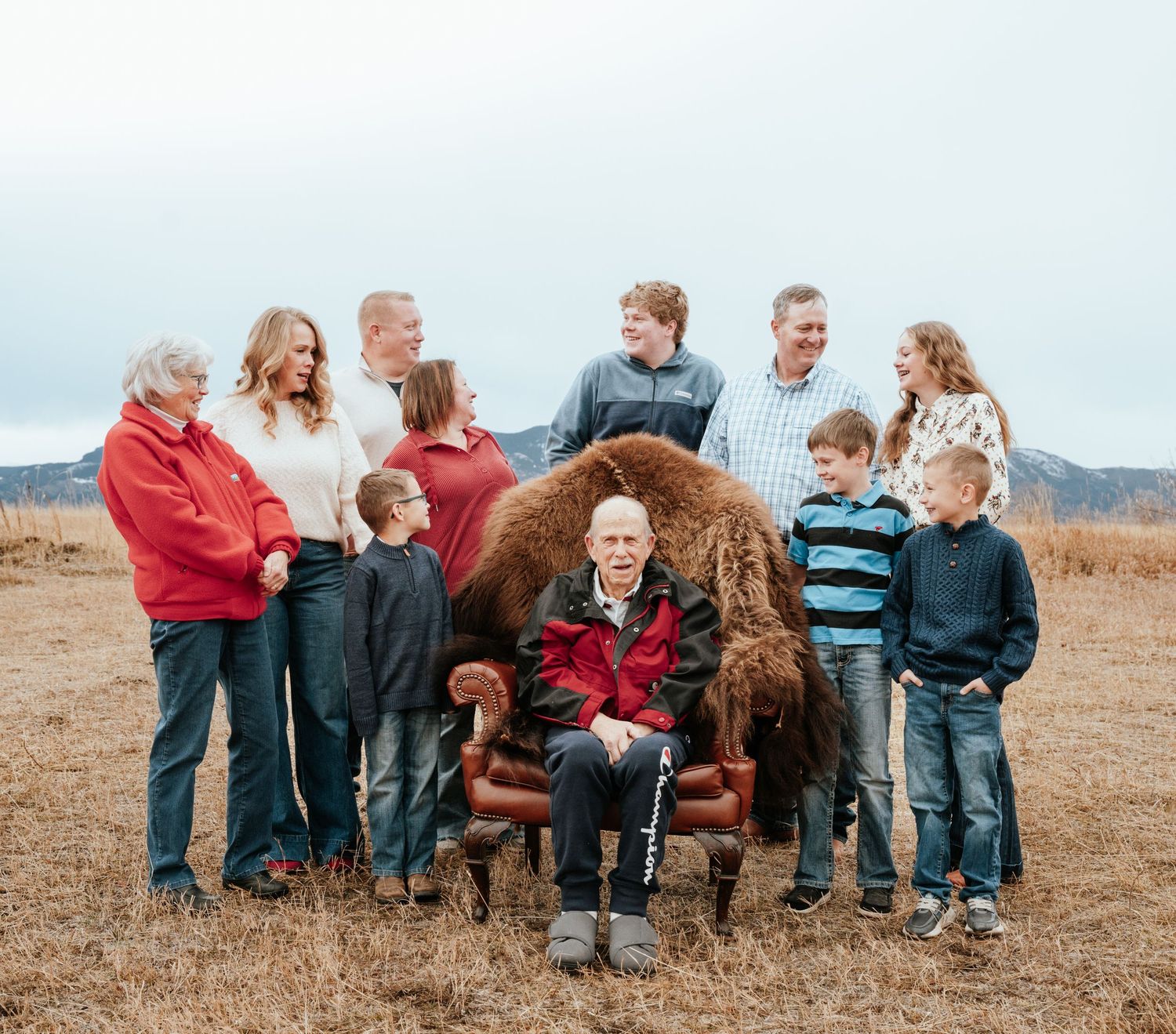 Full family posing with grandfather sitting the middle in a chair.