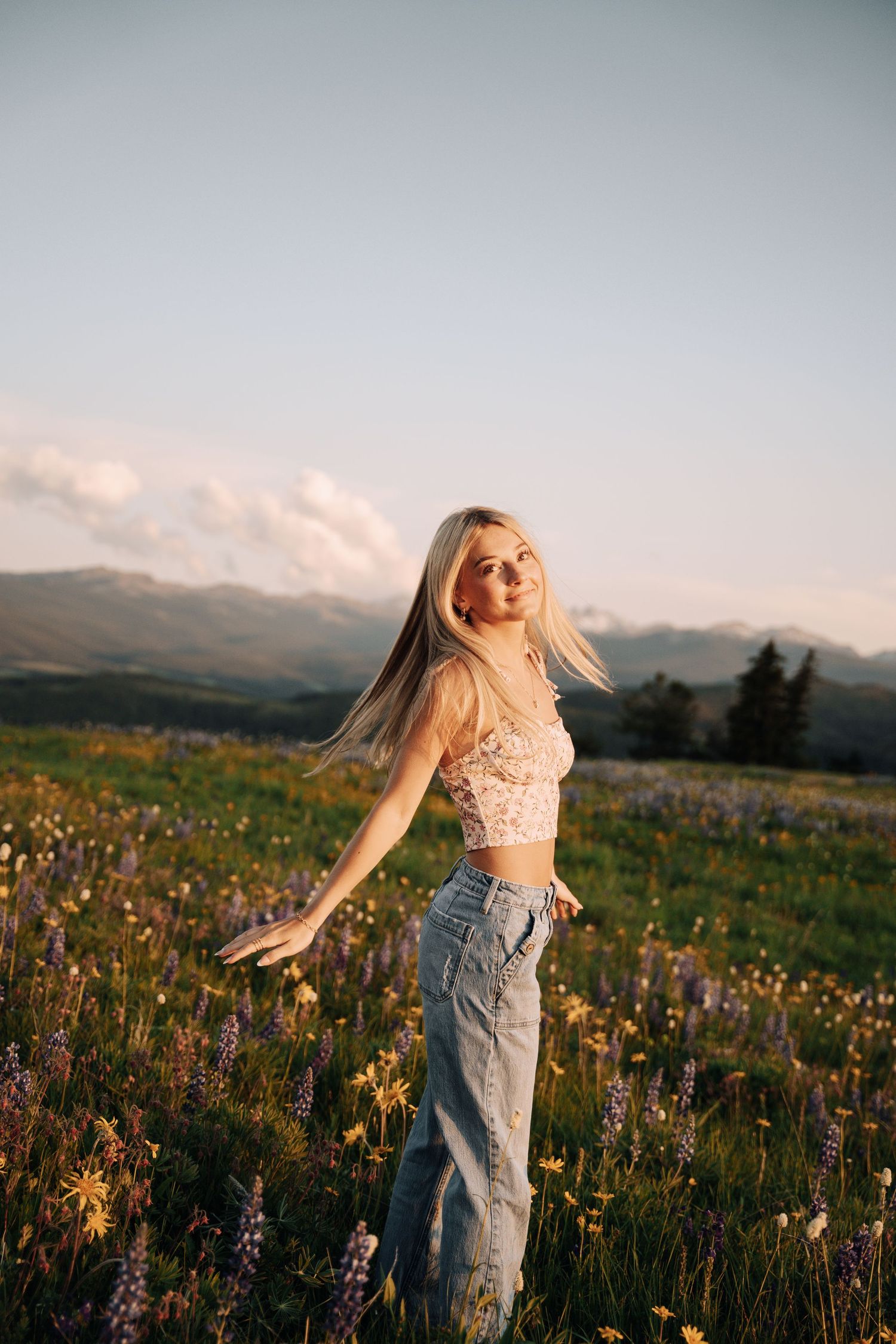 Girl twirling in a flower field with mountains in the background.