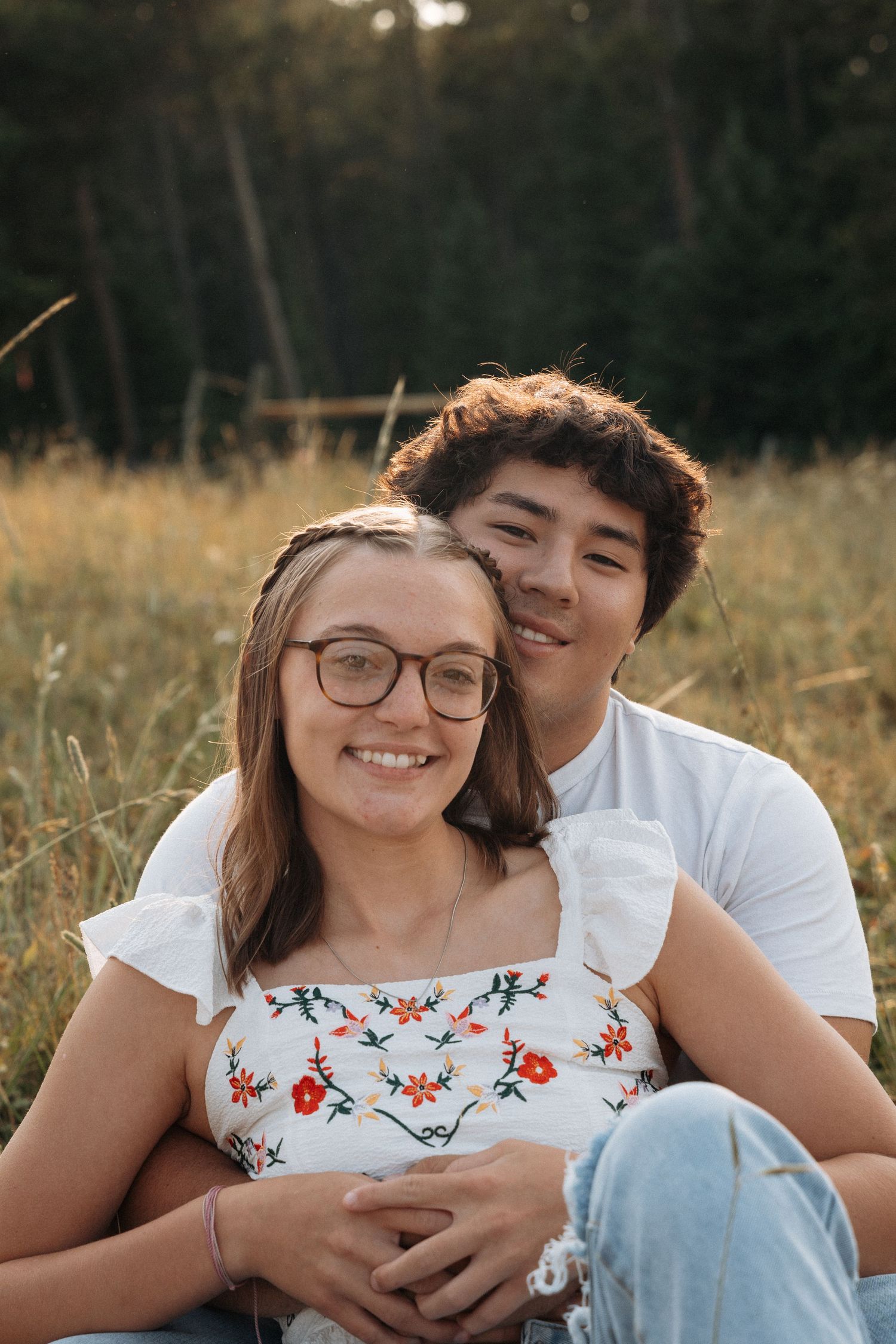 Girlfriend posing with boyfriend in field with sun in the back.