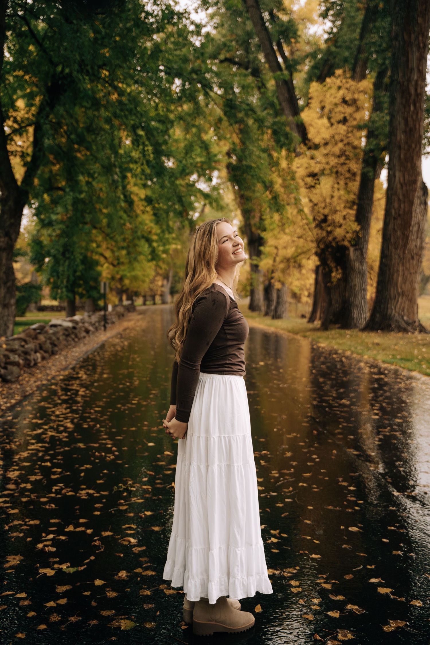 Girl standing in the middle of a road while fall colors surround her and rain falls.