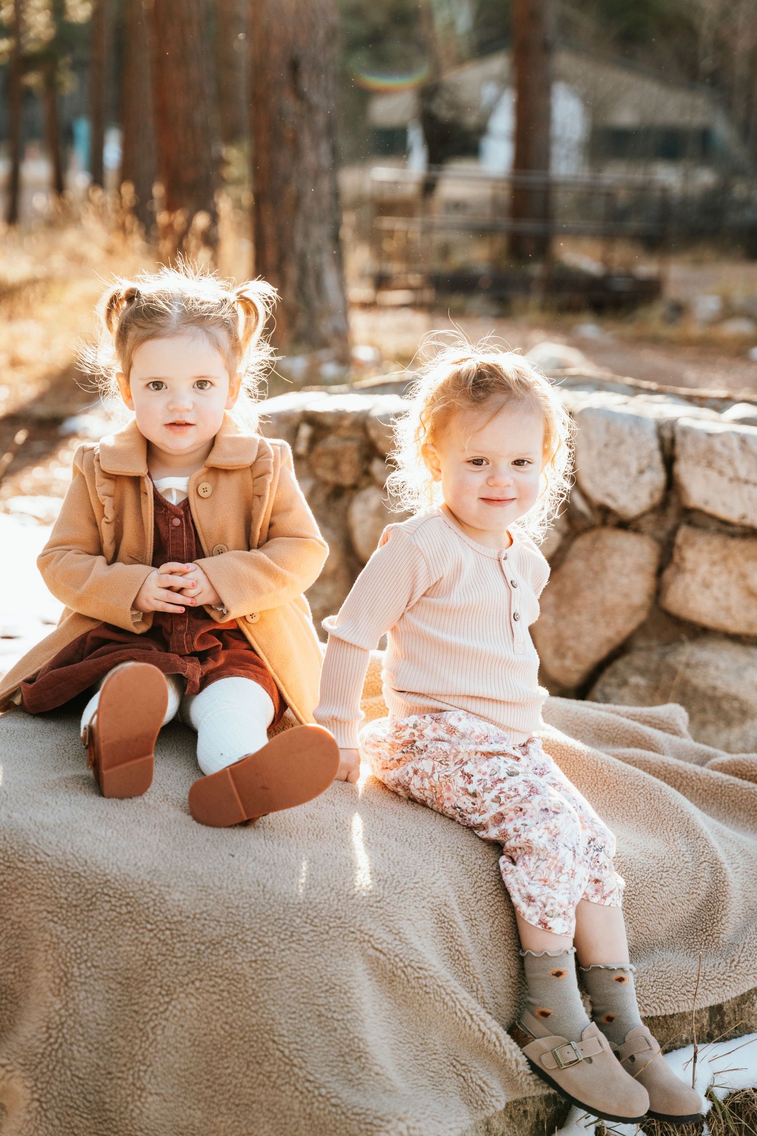 Two children sitting on a rock covered with a blanket.