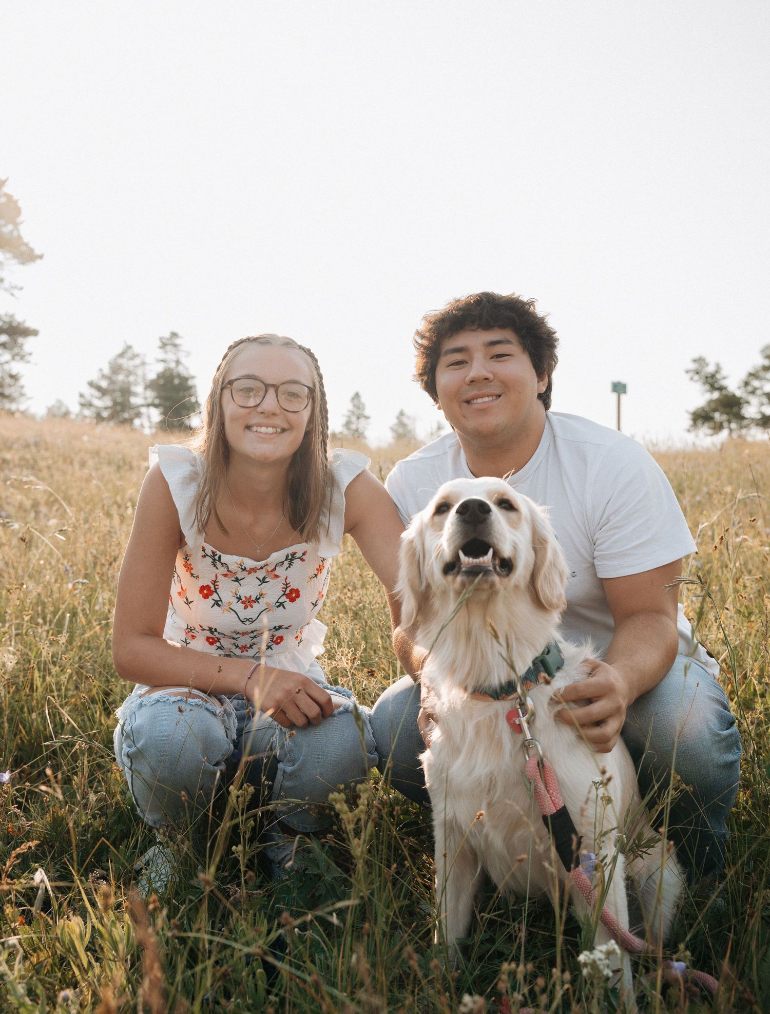 Girlfriend posing with boyfriend in field with sun in the back.