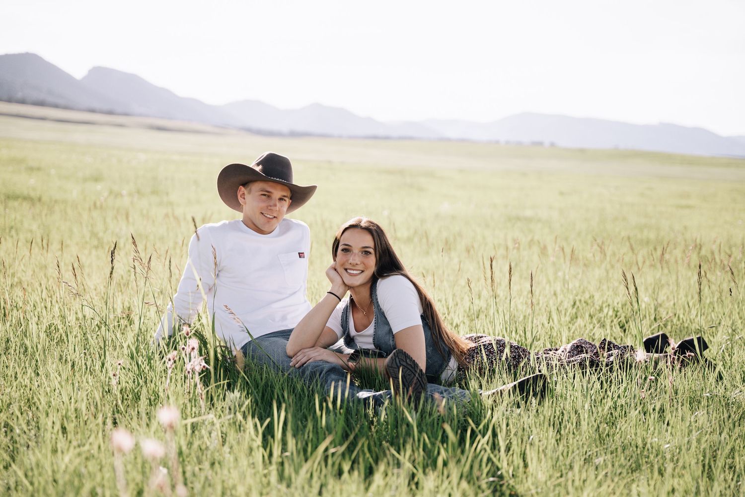 Girlfriend posing with boyfriend in field with sun in the back.