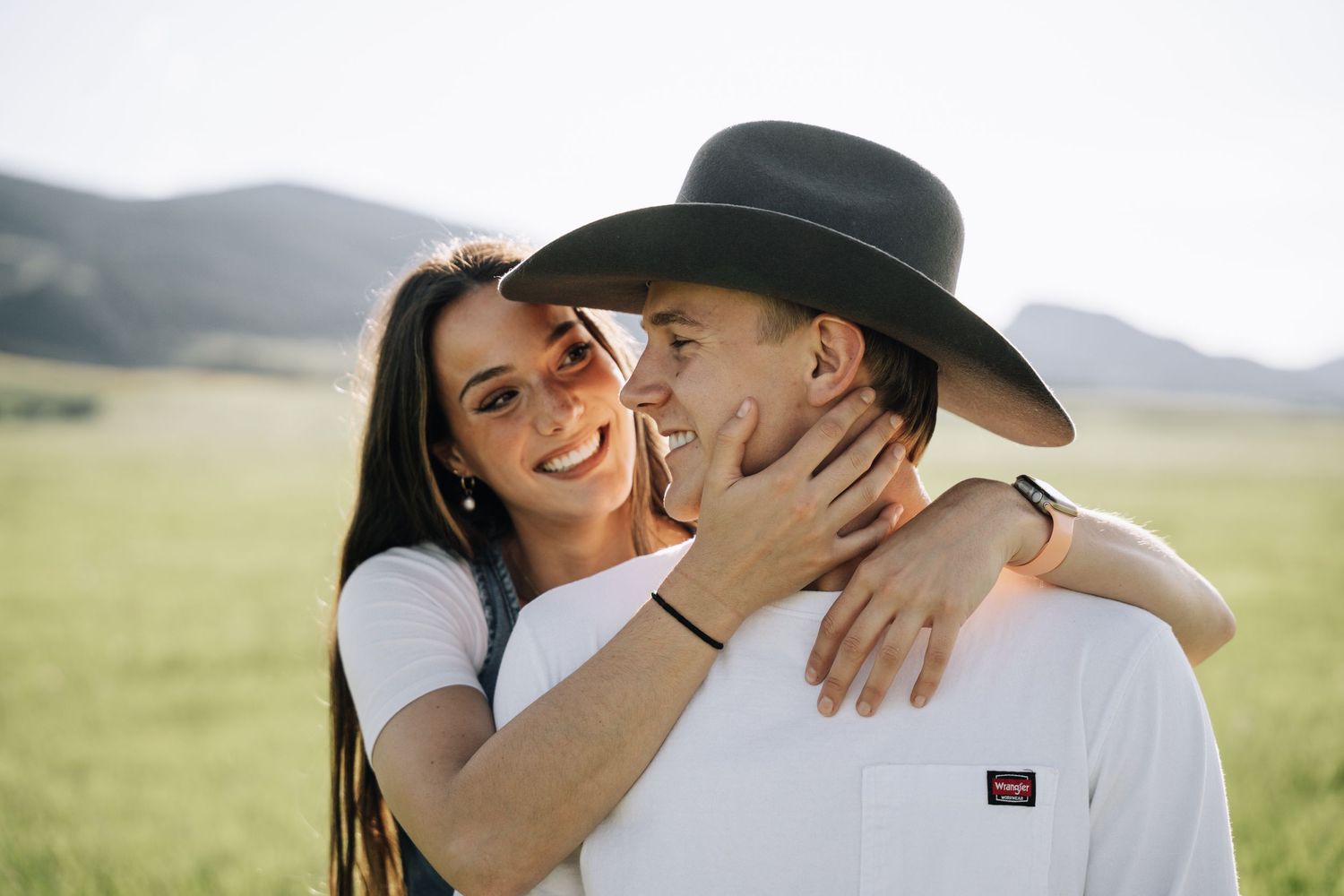 Girlfriend posing with boyfriend in field with sun in the back.