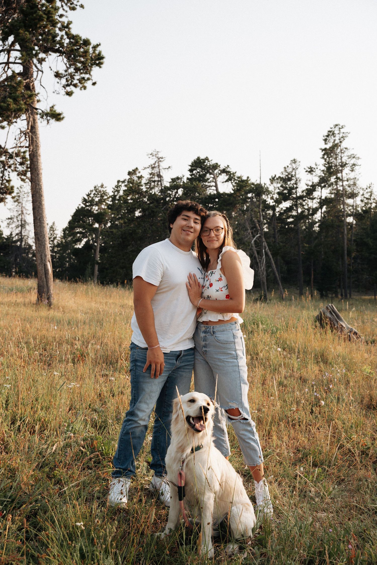 Girlfriend posing with boyfriend in field with sun in the back.