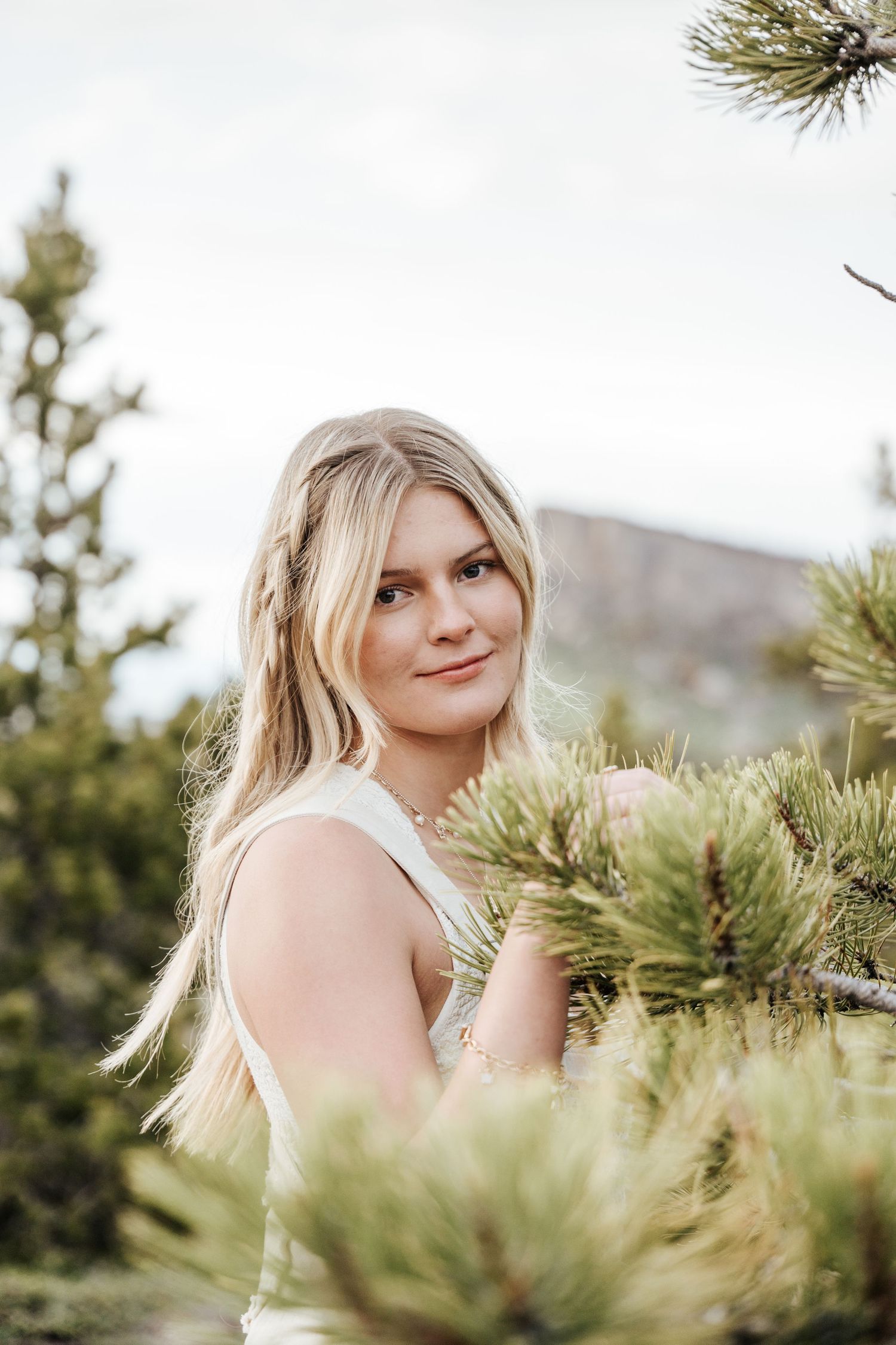 Girl looking at the camera through a tree with a mountain in the back.