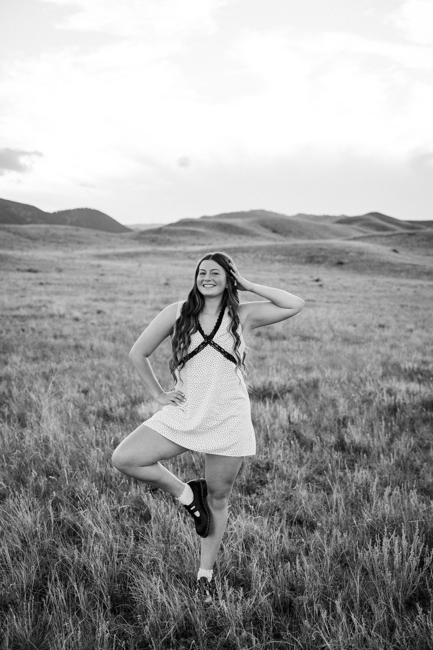 Girl posing in the middle of a field with mountains in the background.