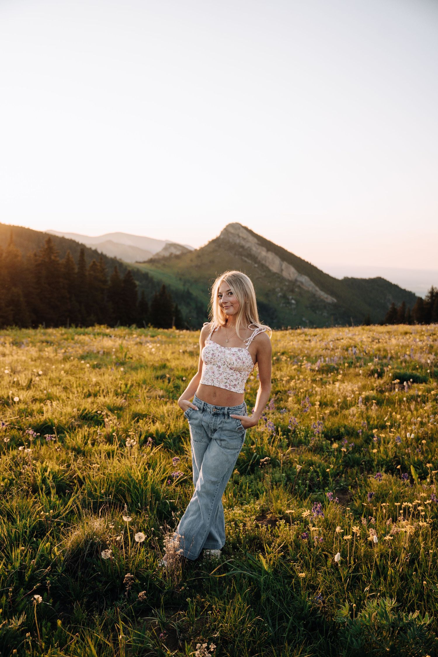 Girl standing with hands in her pockets in front of a mountain.