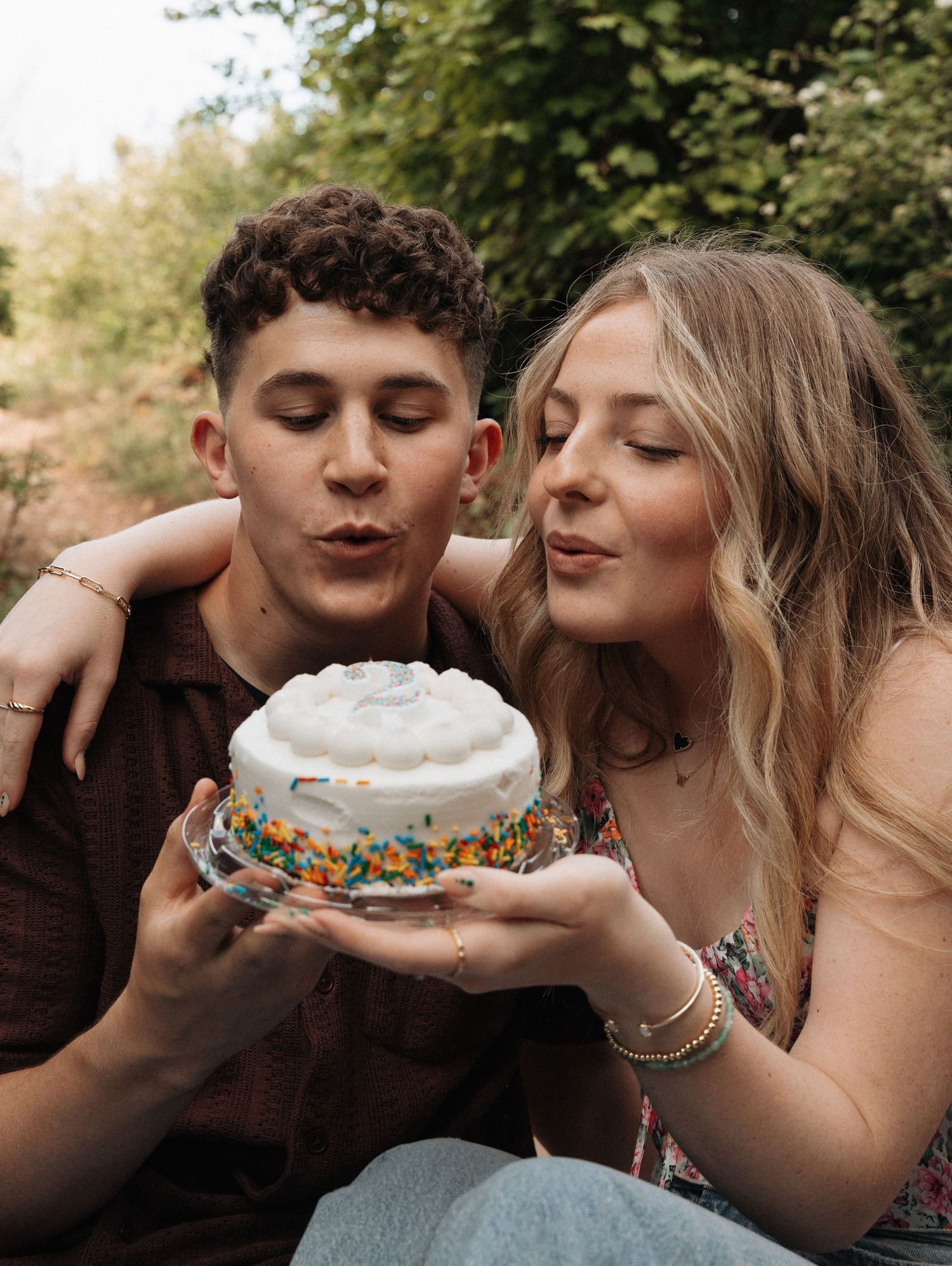 Girlfriend posing with boyfriend on bridge blowing out candle on a cake.