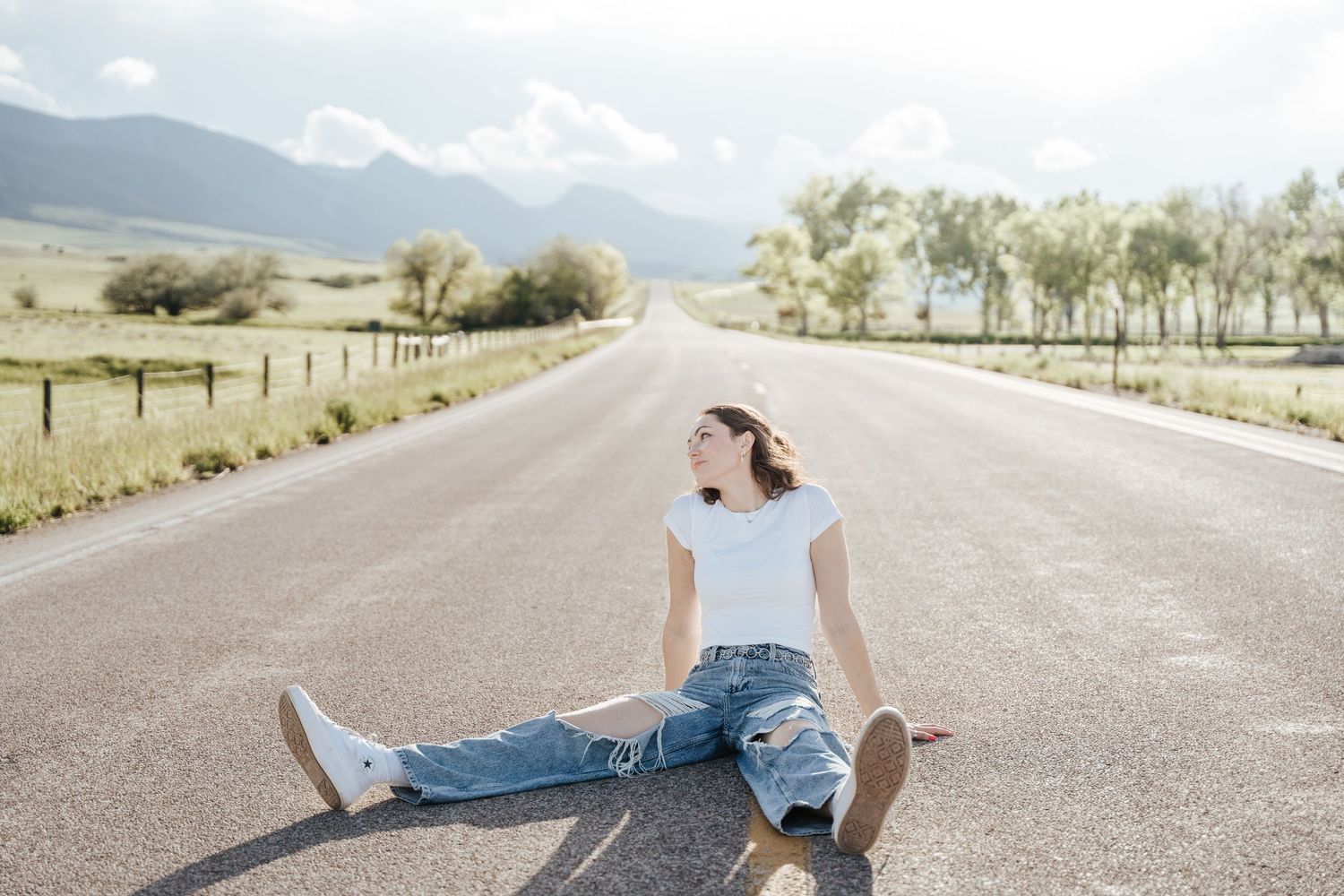 Girl sitting in the middle of a road while looking away.