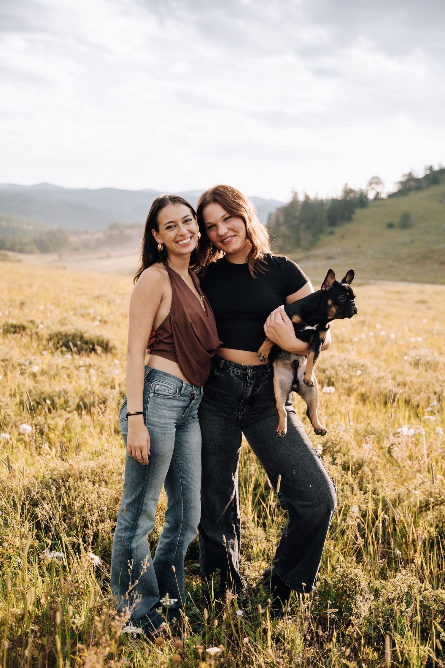 Two girls standing together, one holding a dog