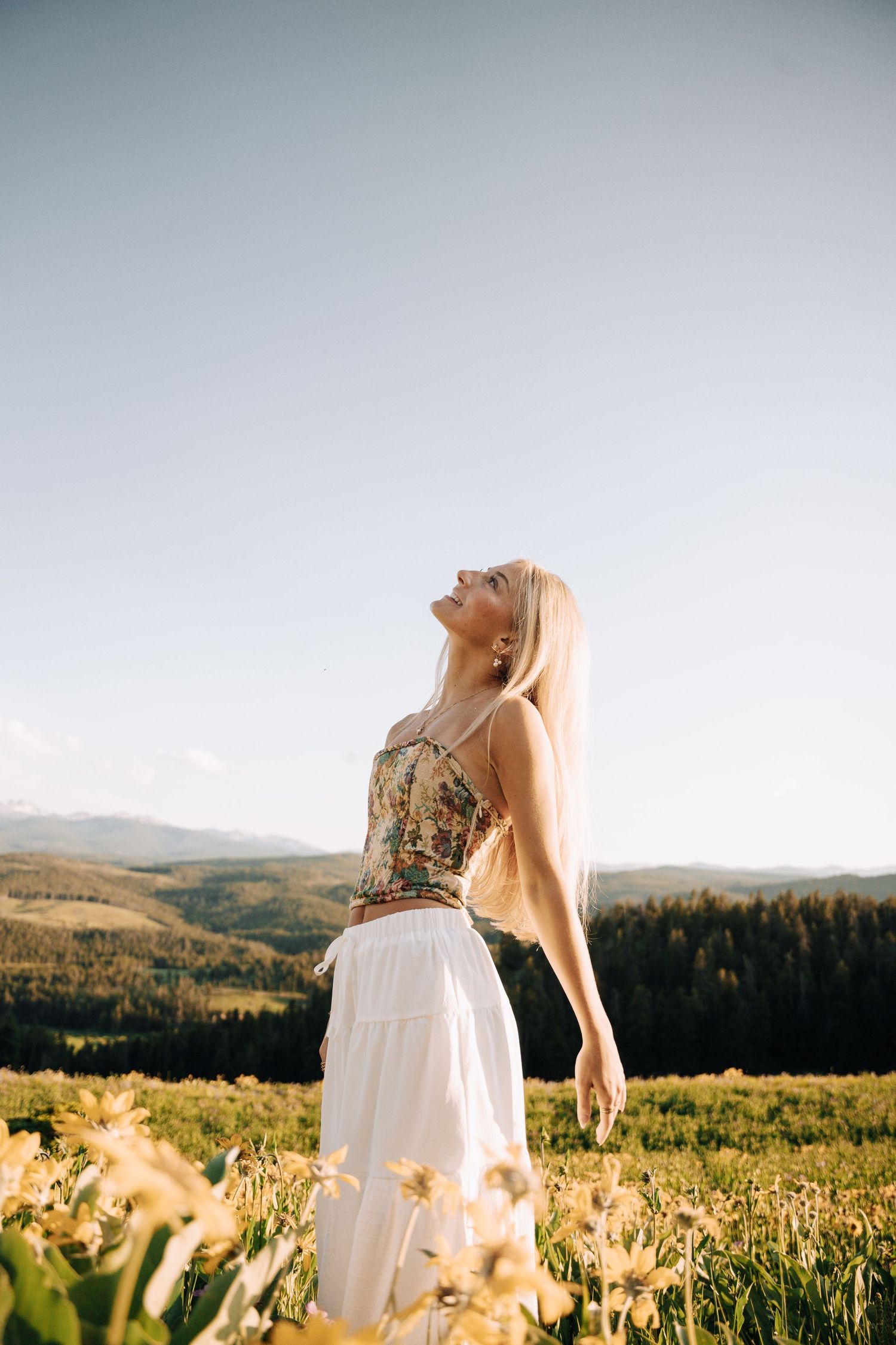 Girl in the middle of a yellow flower field. Mountains and open green spaces in the background.