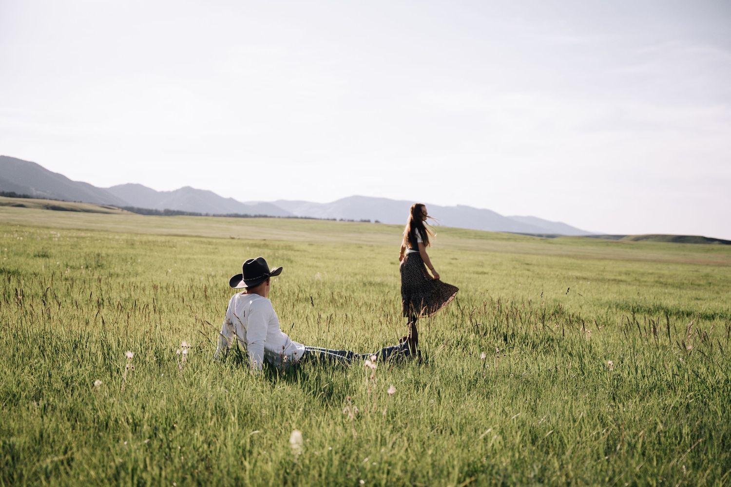 Girlfriend posing with boyfriend in field with sun in the back.