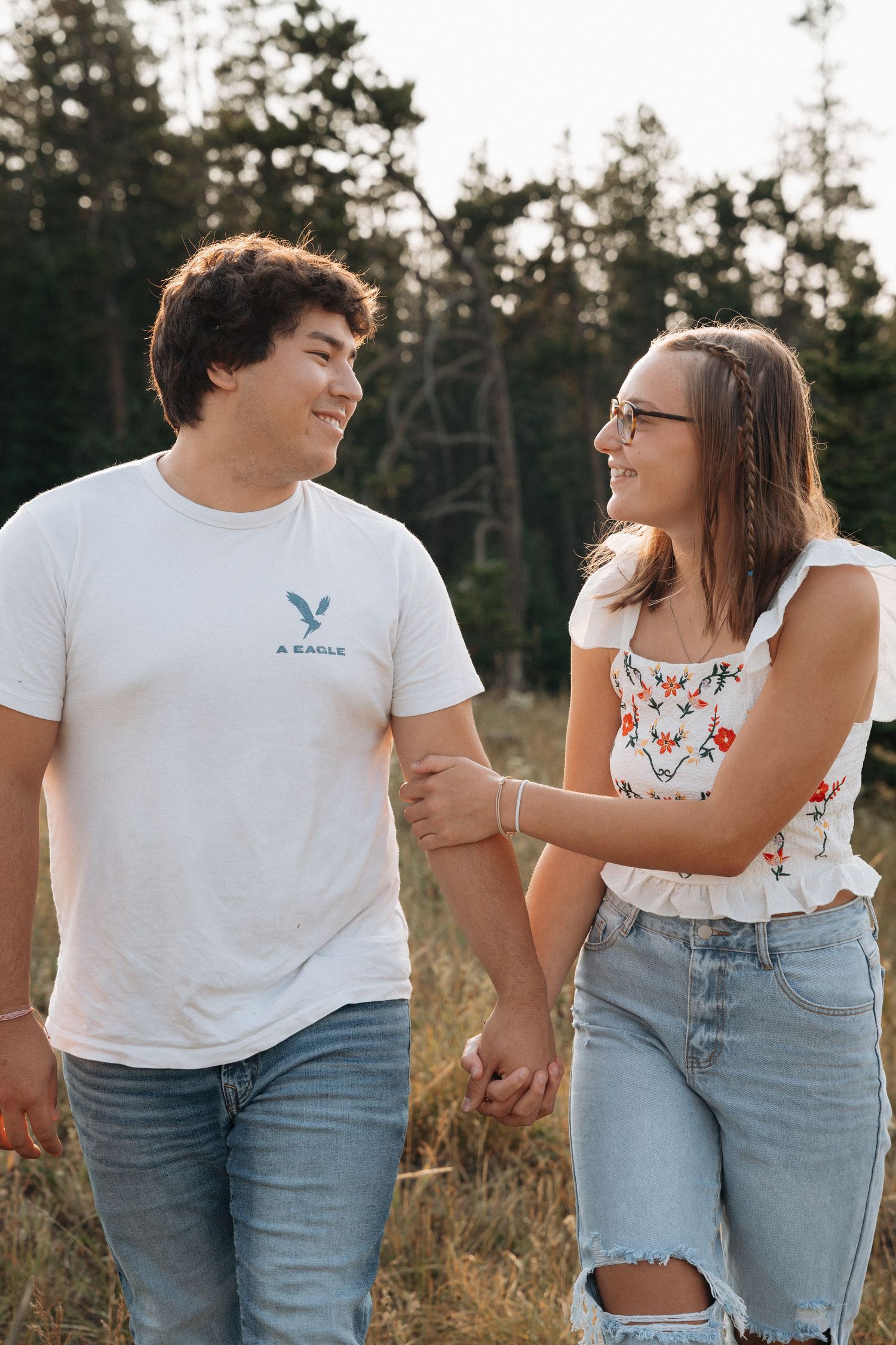 Girlfriend posing with boyfriend in field with sun in the back.