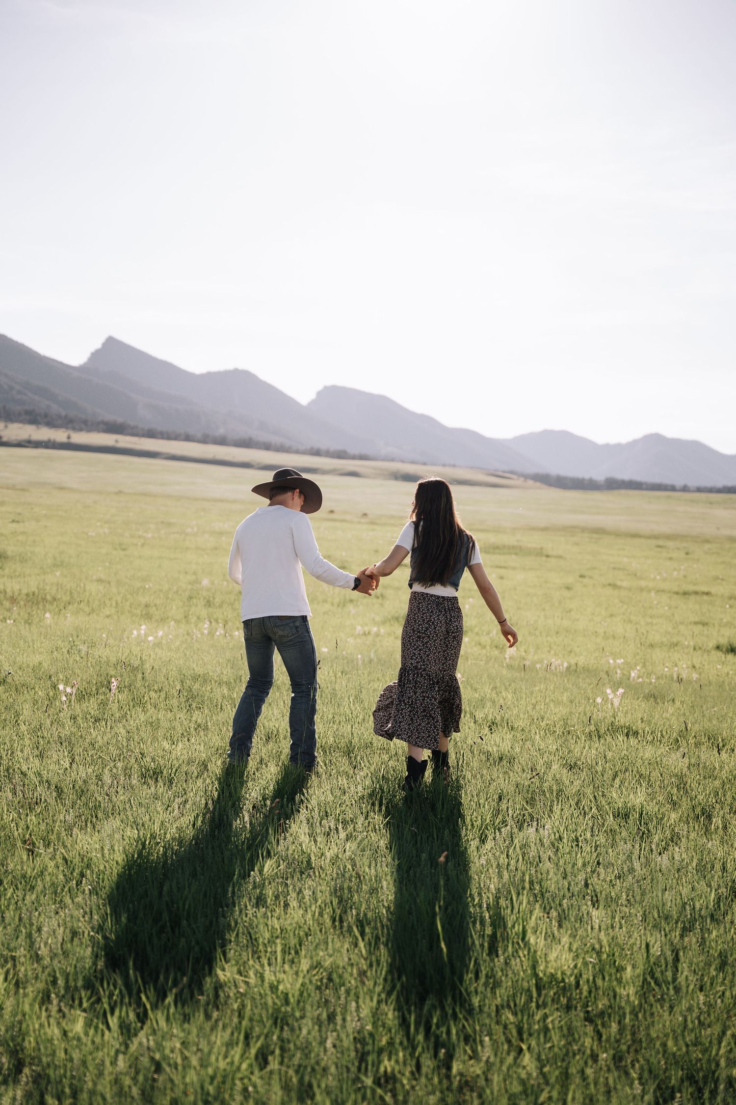 Girlfriend posing with boyfriend in field with sun in the back.
