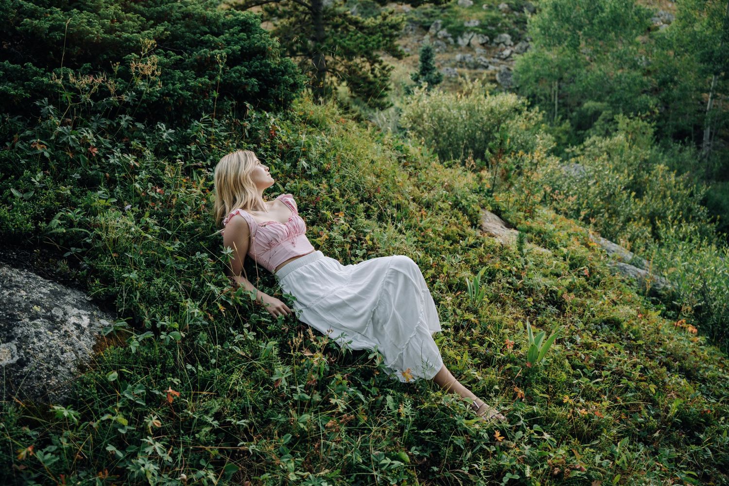 Girl laying on a green hill looking away from the camera.