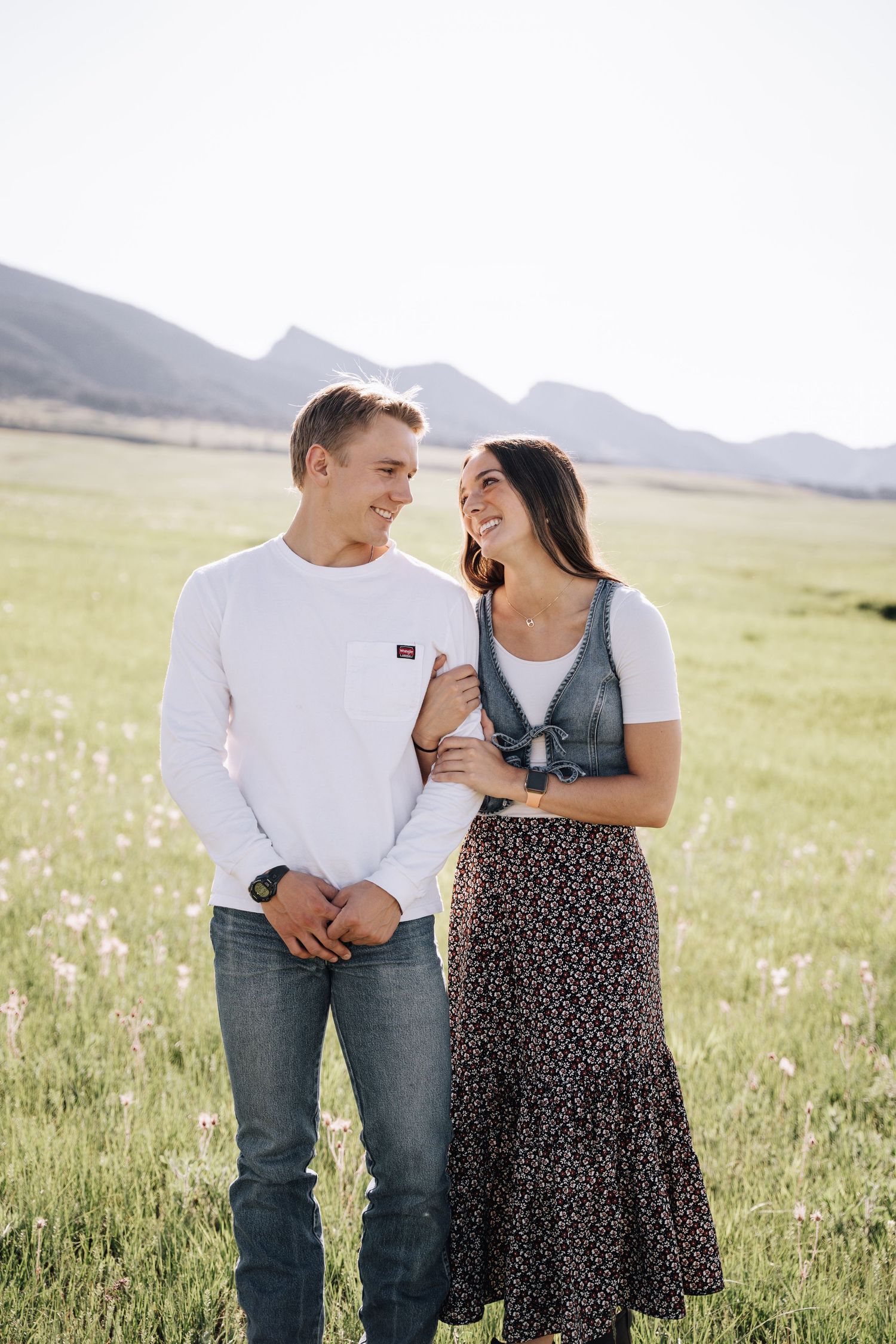 Girlfriend posing with boyfriend in field with sun in the back.