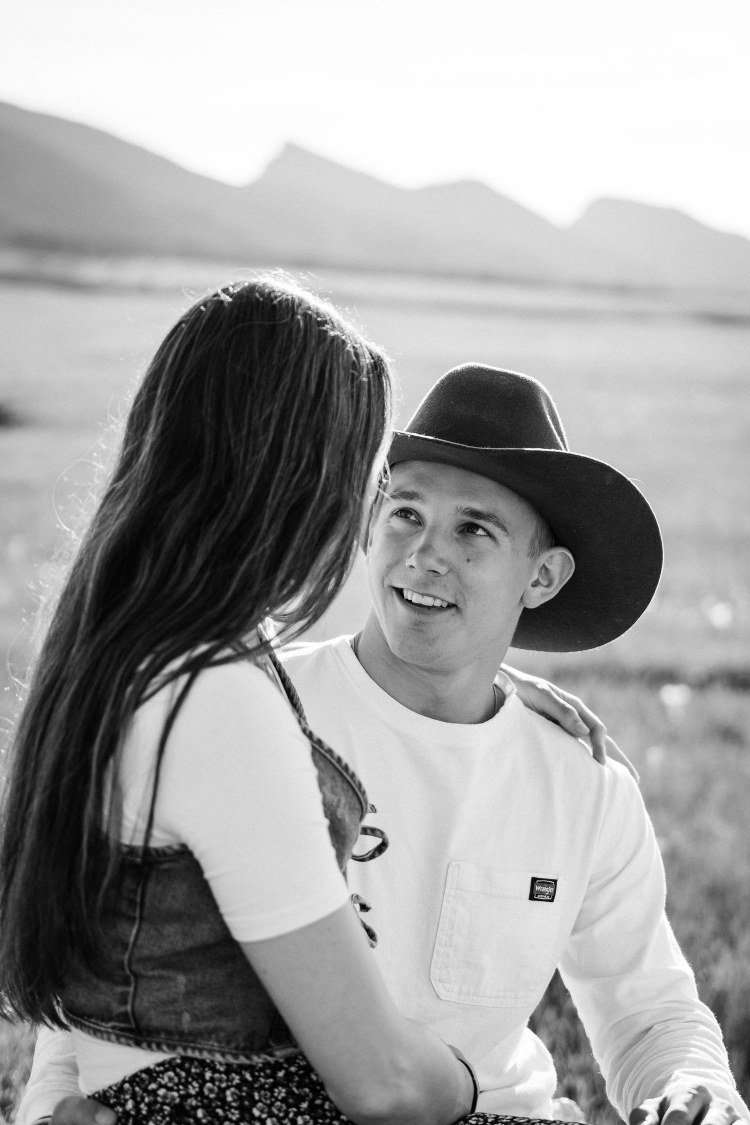Girlfriend posing with boyfriend in field with sun in the back.
