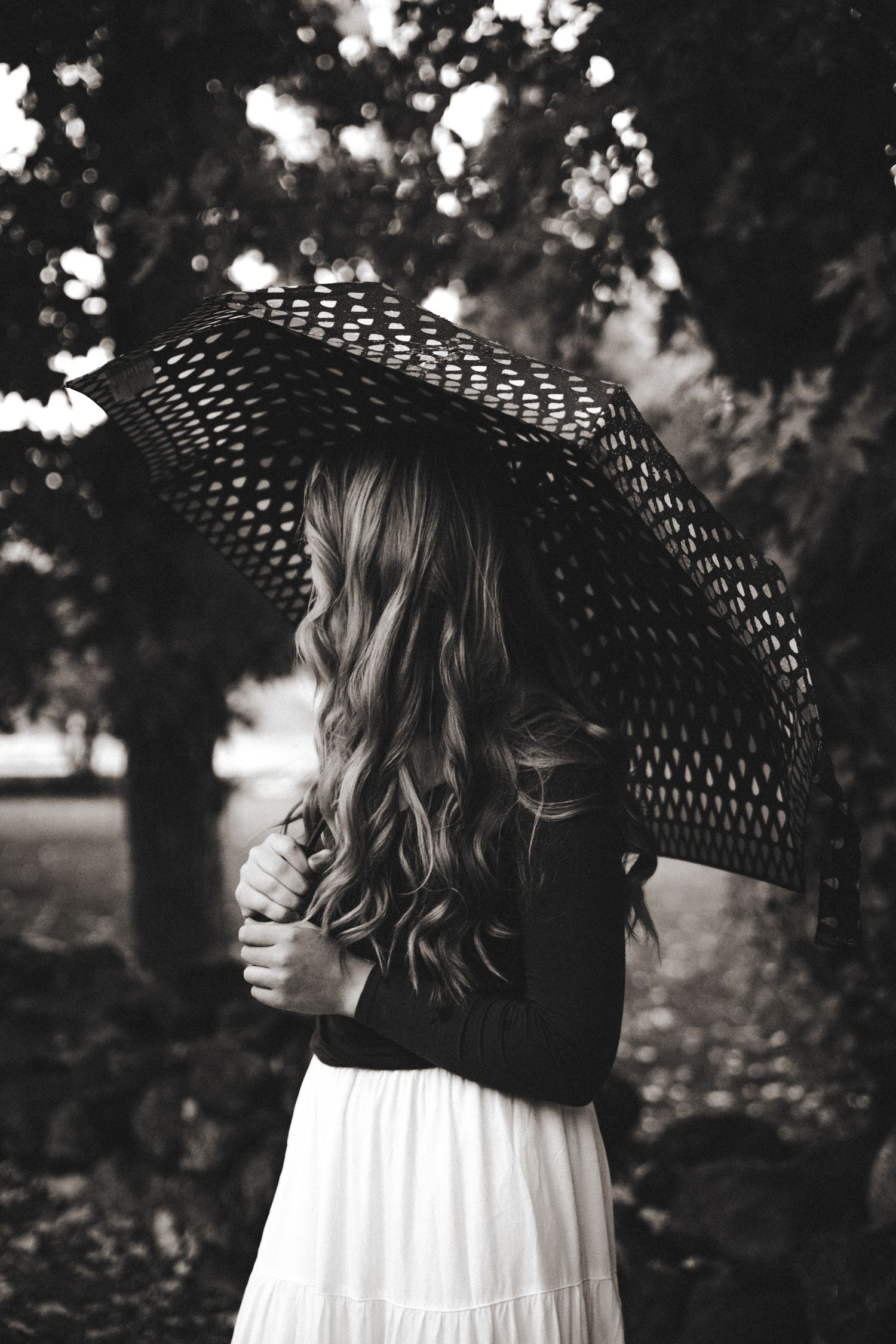 Black and white photo of a girl holing an umbrella in the rain.