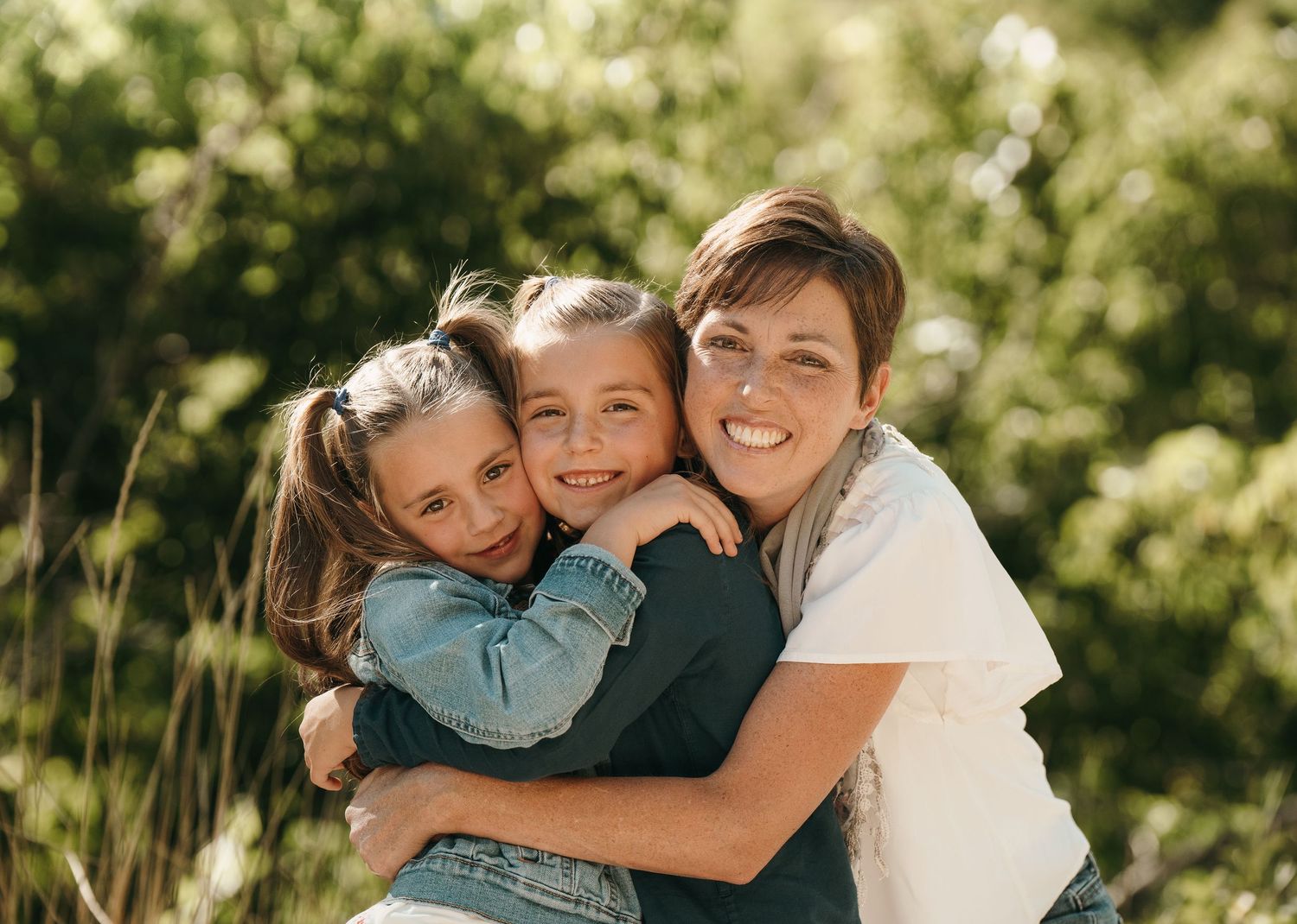 Mom posing with her daughters in front of greenery.