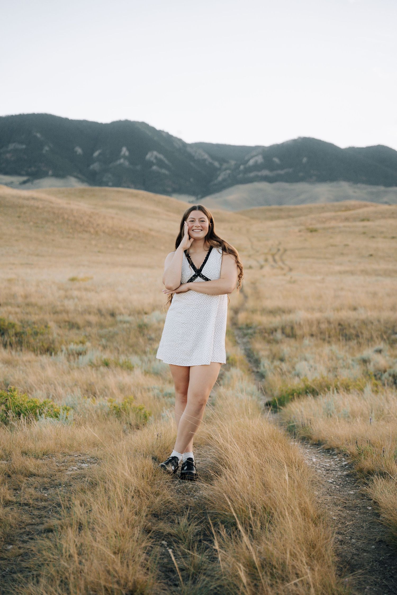 Girl posing in the middle of a field with mountains in the background.