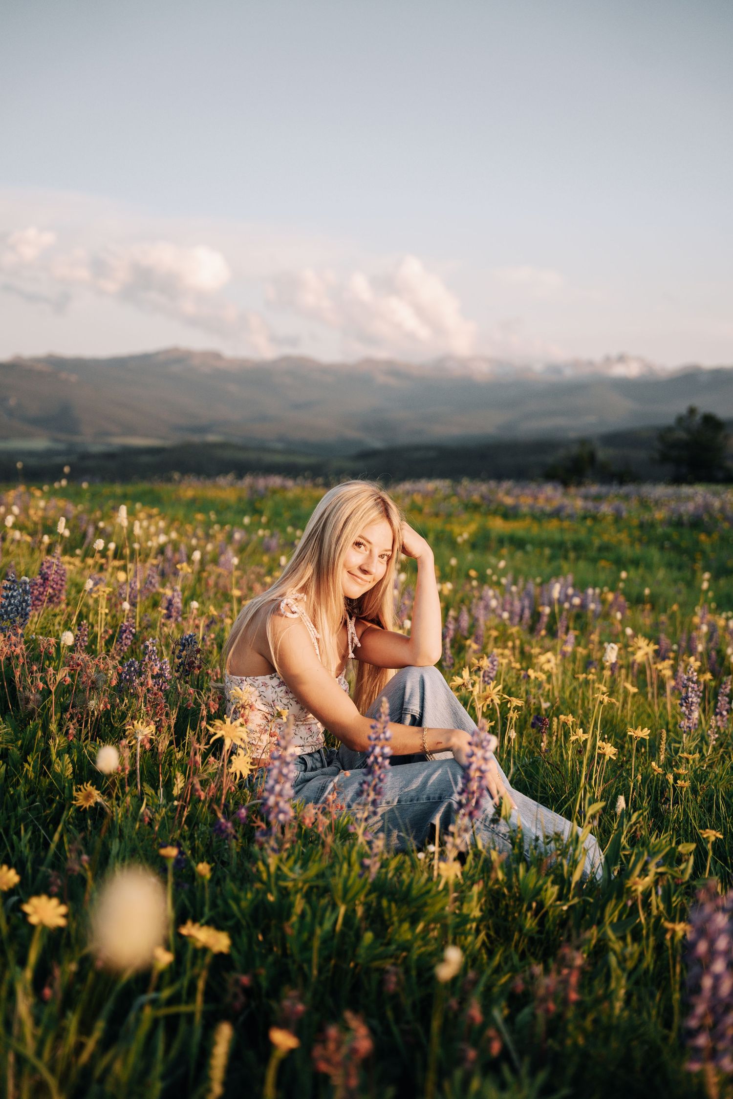 Girl sitting in a flower field and mountains in the background.