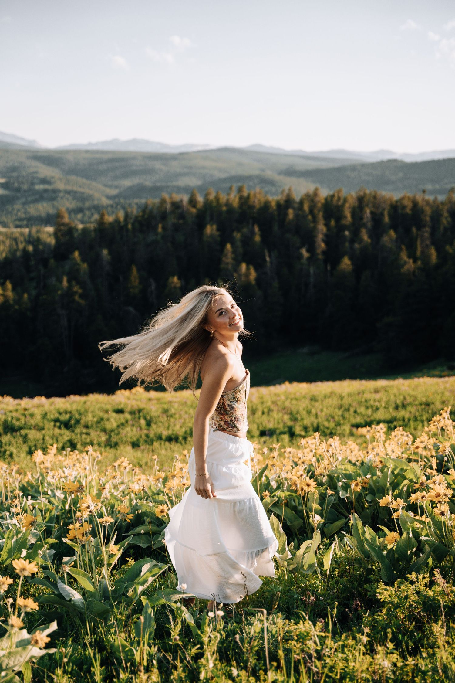 Girl in the middle of a yellow flower field. Mountains and open green spaces in the background.