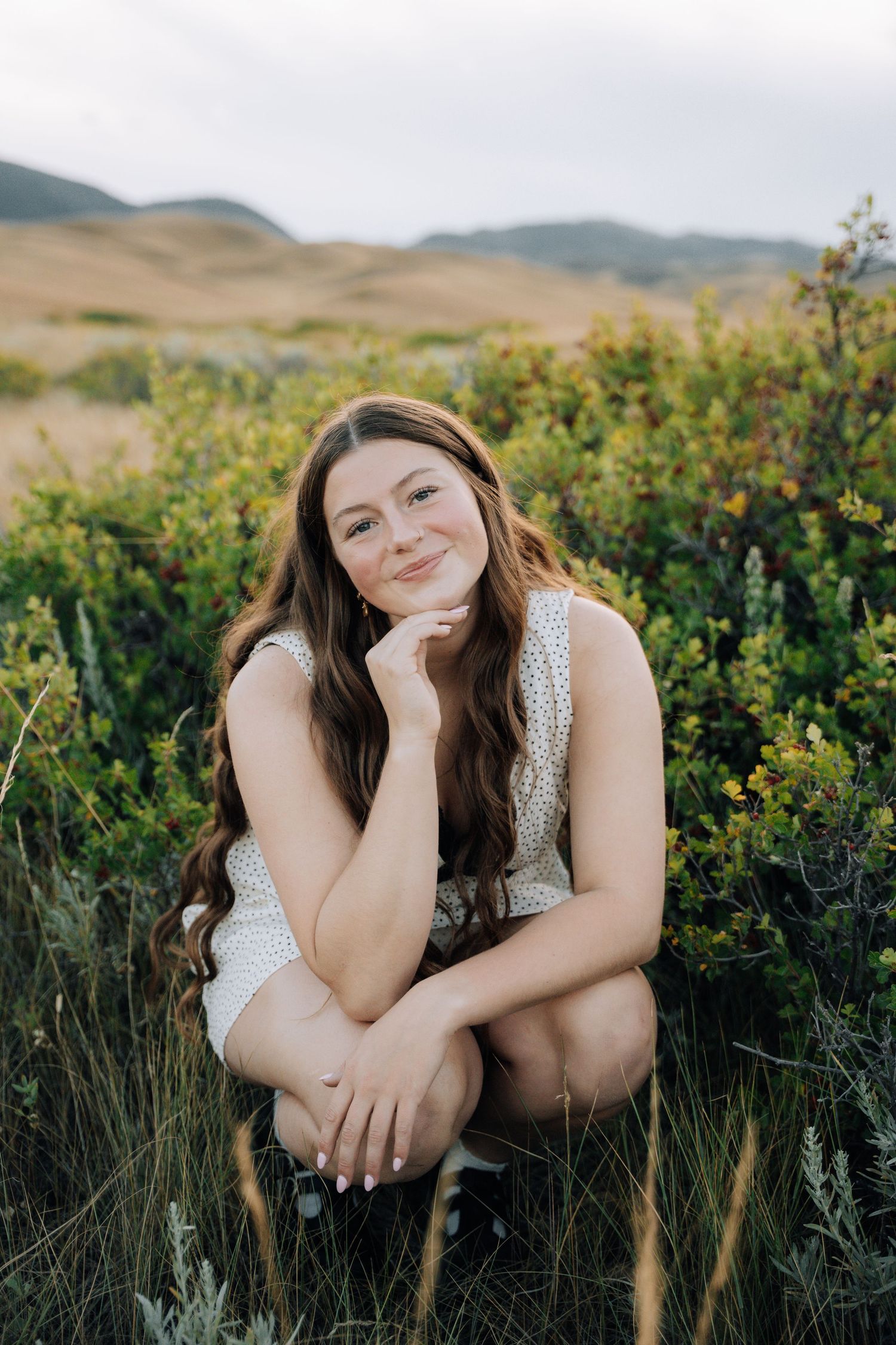 Girl crouching in a green bush holding her head with ehr hand.