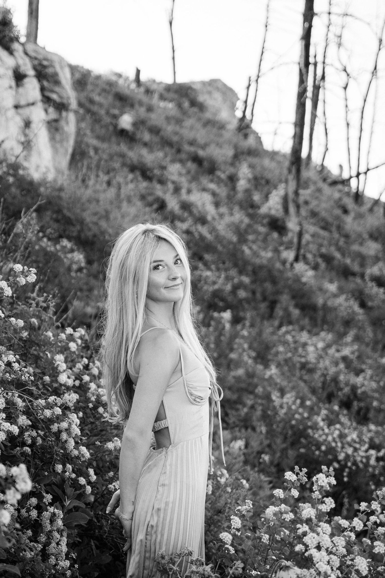 Girl in the middle of a yellow flower field. Mountains and open green spaces in the background.