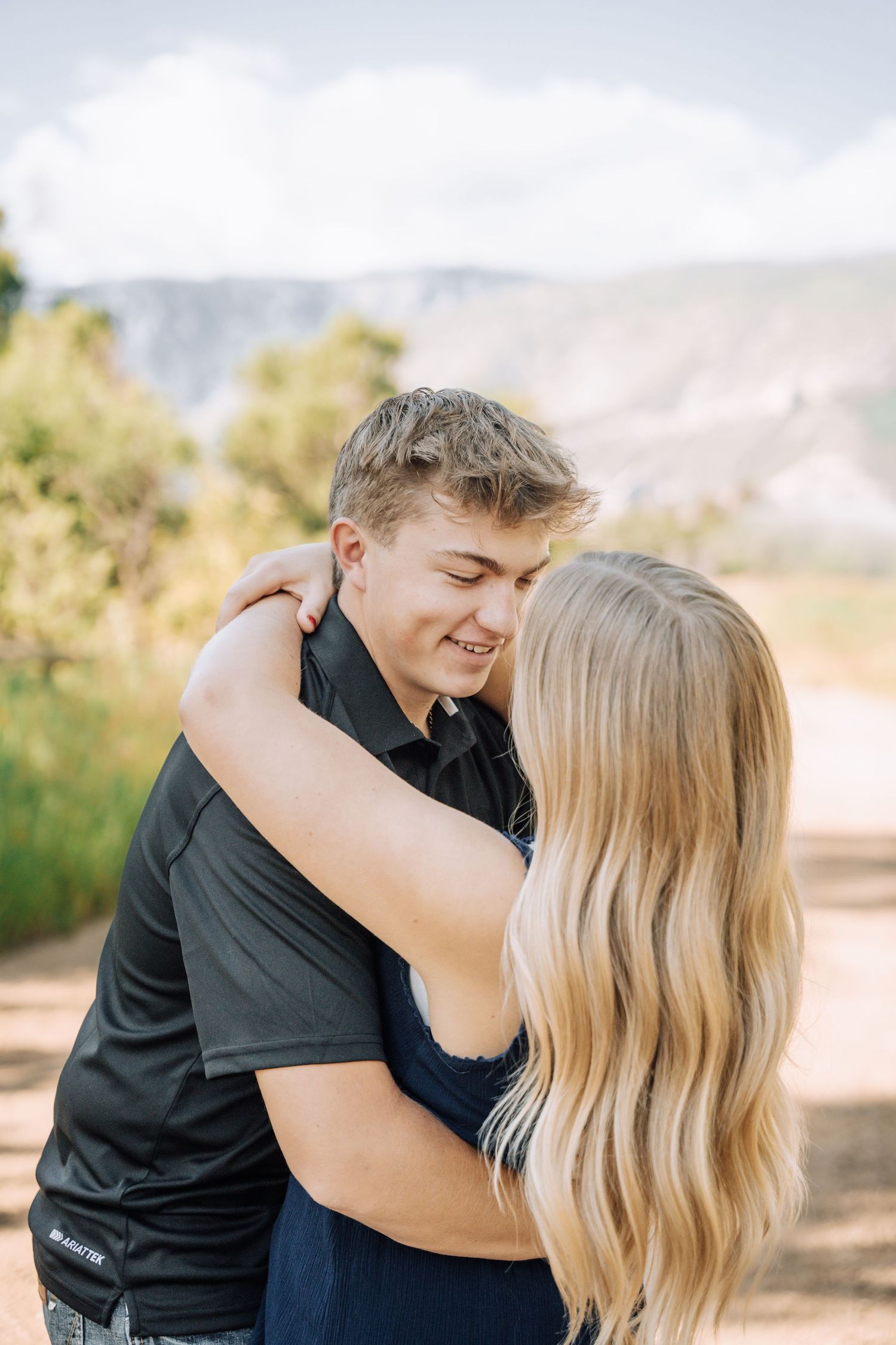 Girlfriend posing with boyfriend in field with sun in the back.