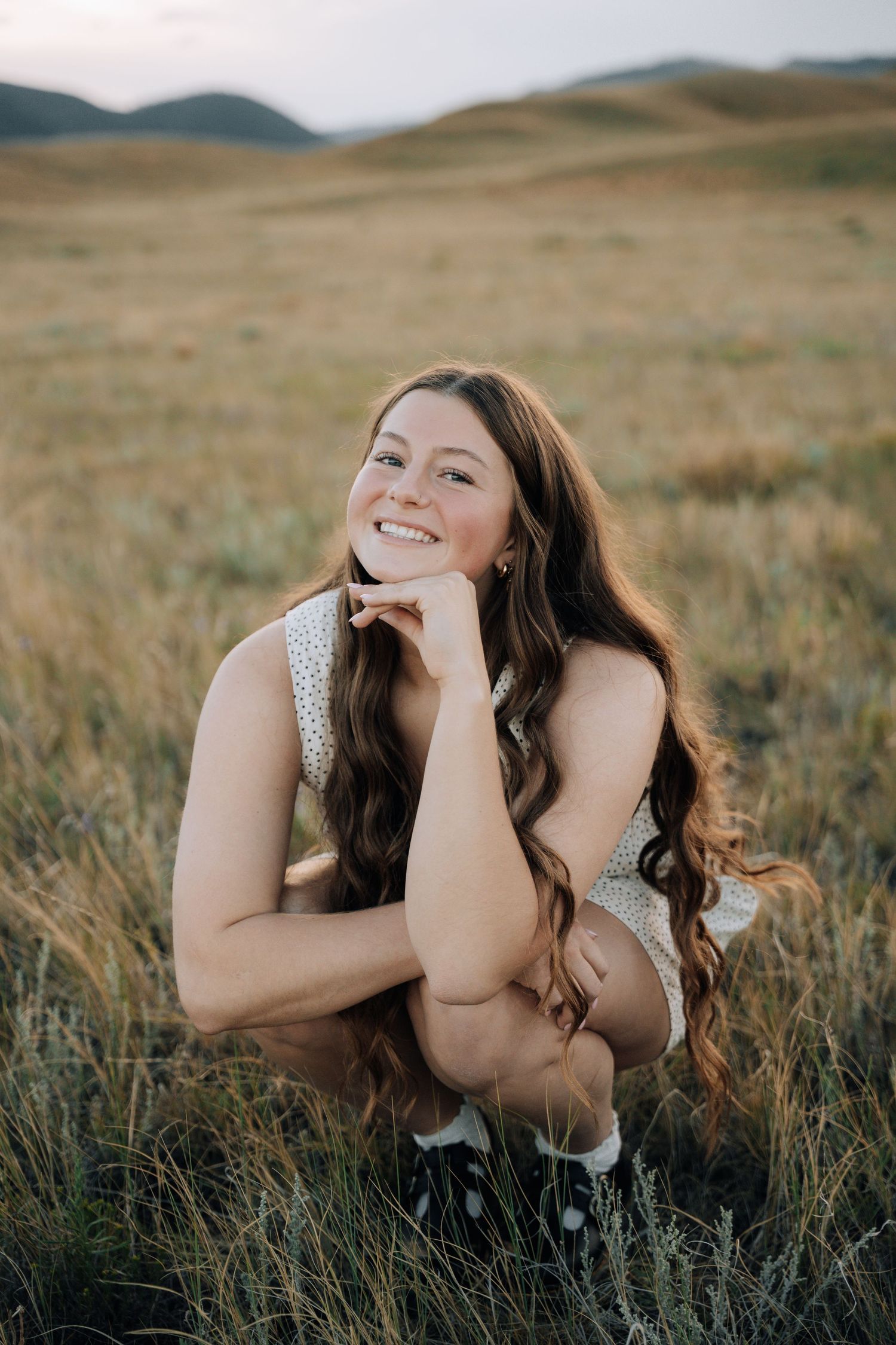 Girl crouching in a green bush holding her head with ehr hand.