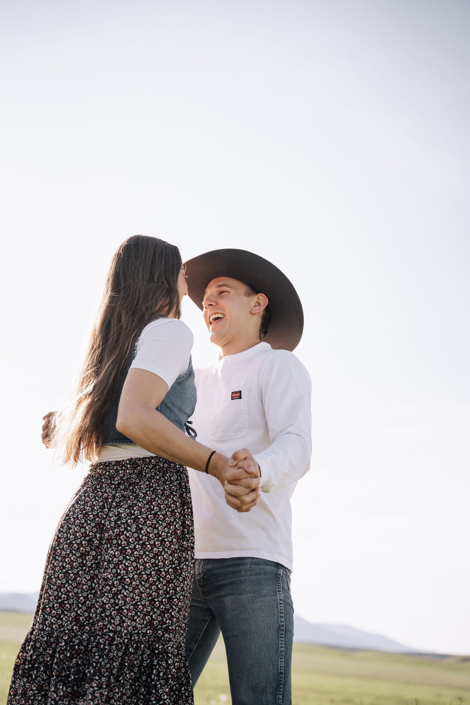 Girlfriend posing with boyfriend in field with sun in the back.