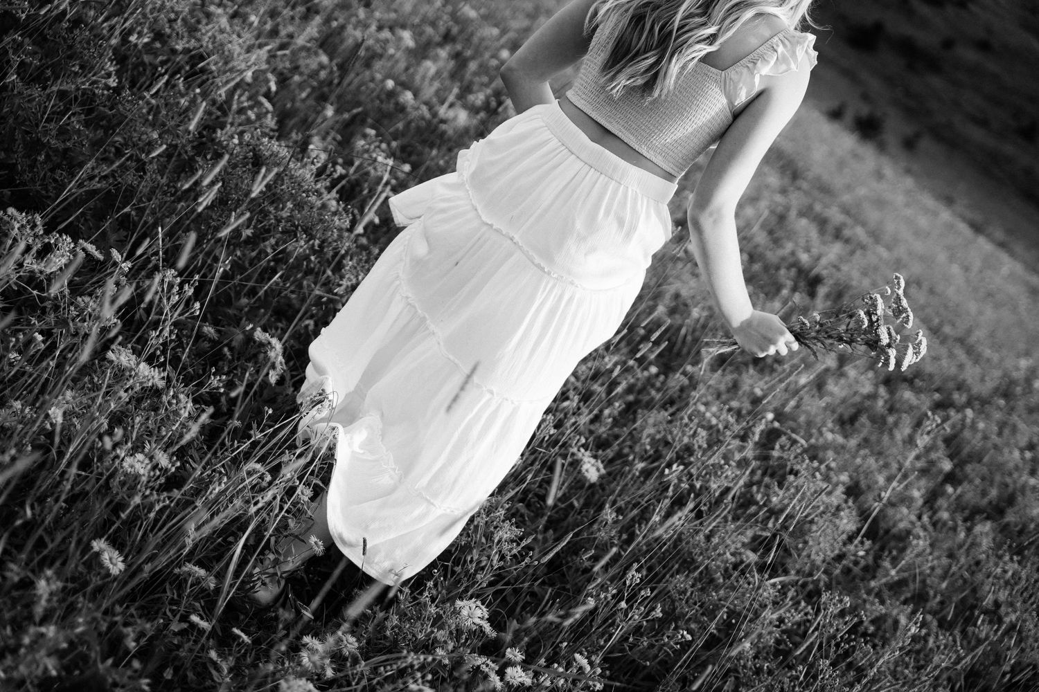 Candid photo of a girl walking away from the camera holding her skirt and a flower.