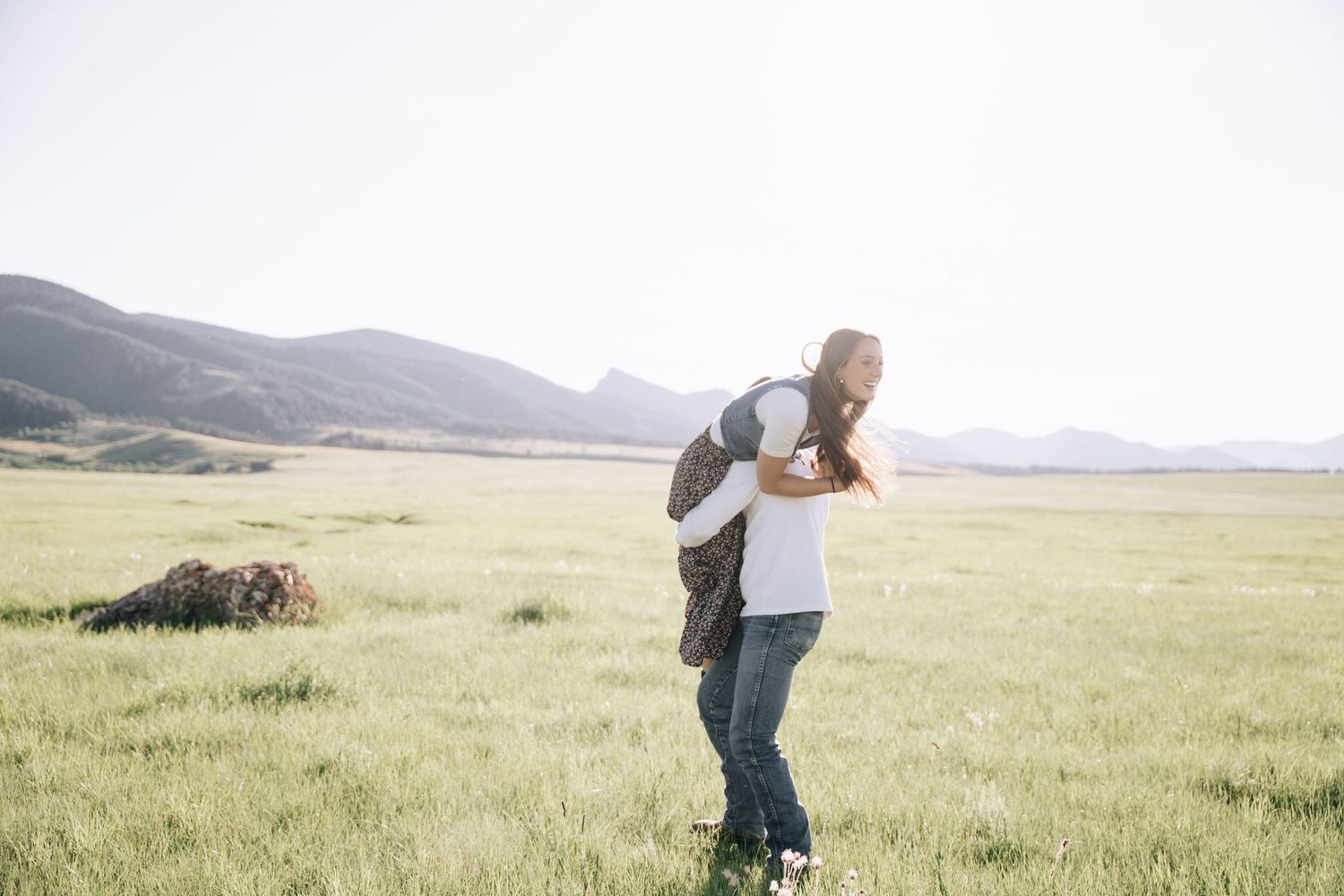Girlfriend posing with boyfriend in field with sun in the back.