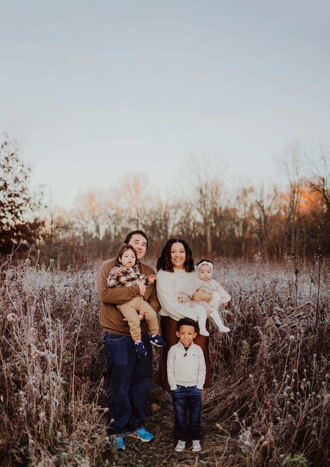A family portrait taken in a field of tall grass during golden hour at sunset.