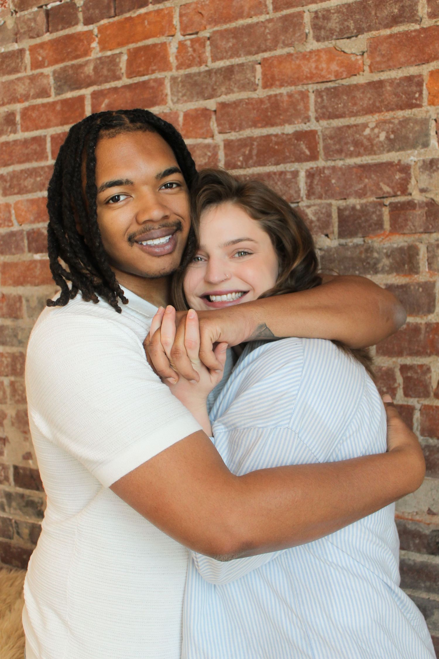 Couple shares an intimate embrace while posing against a rustic brick wall background.