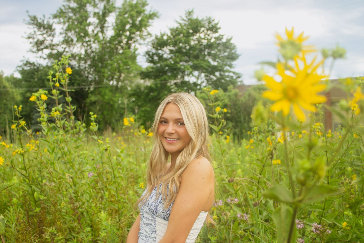 Person in white sundress standing in vibrant field of yellow wildflowers on sunny summer day.