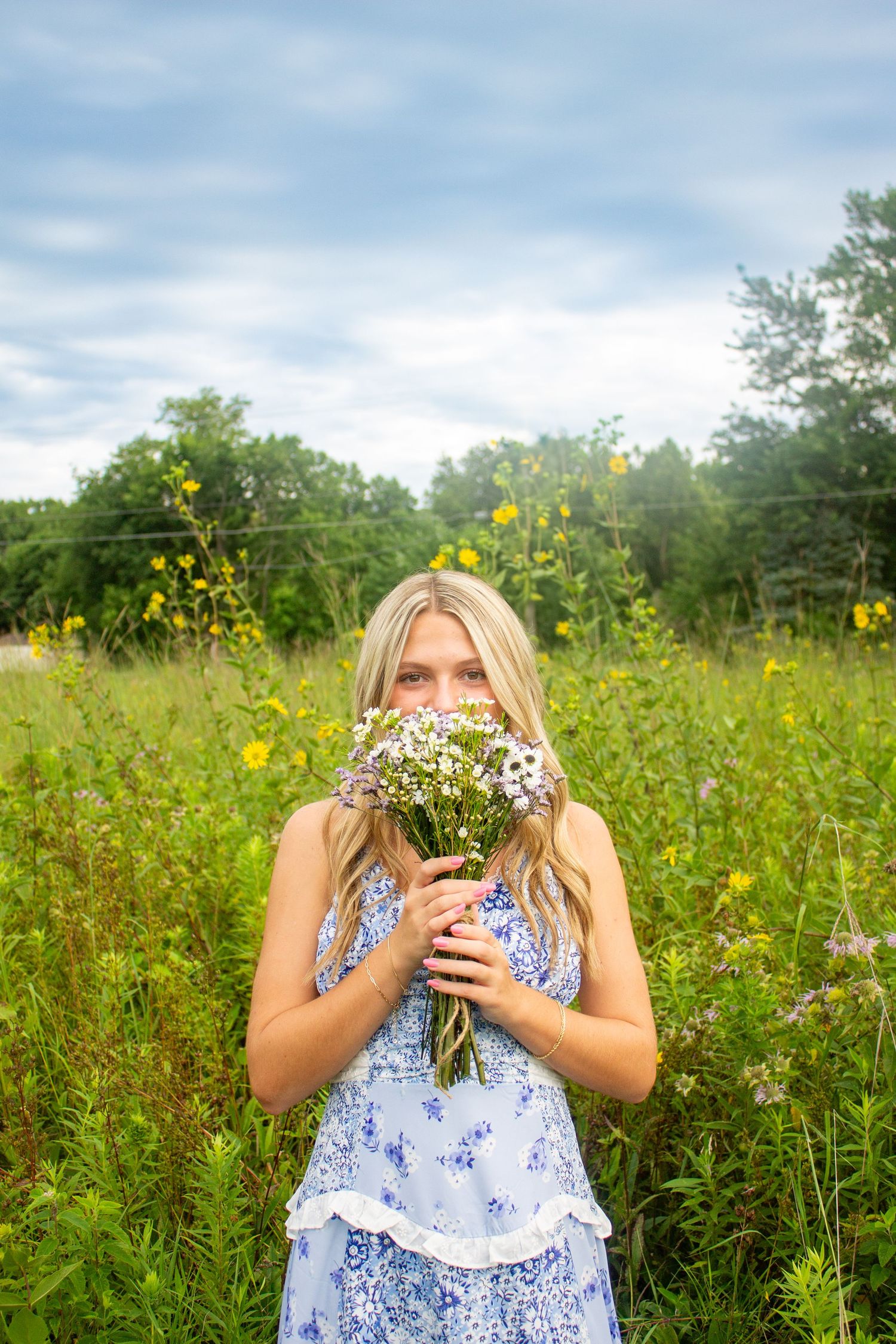 Person in blue floral dress surrounded by blooming wildflowers and tall grass.