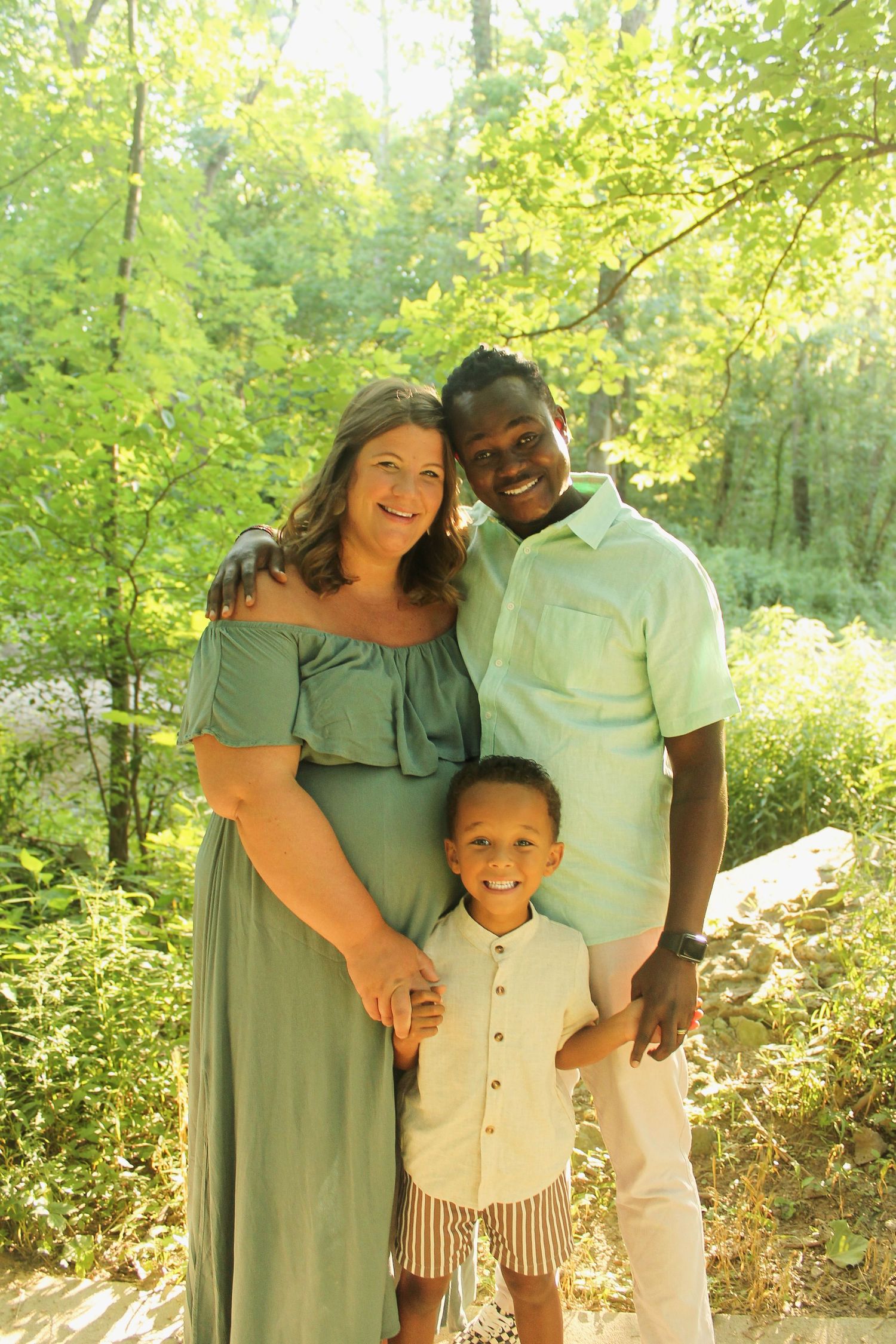 Family of three poses together in nature wearing coordinated mint green and white outfits.