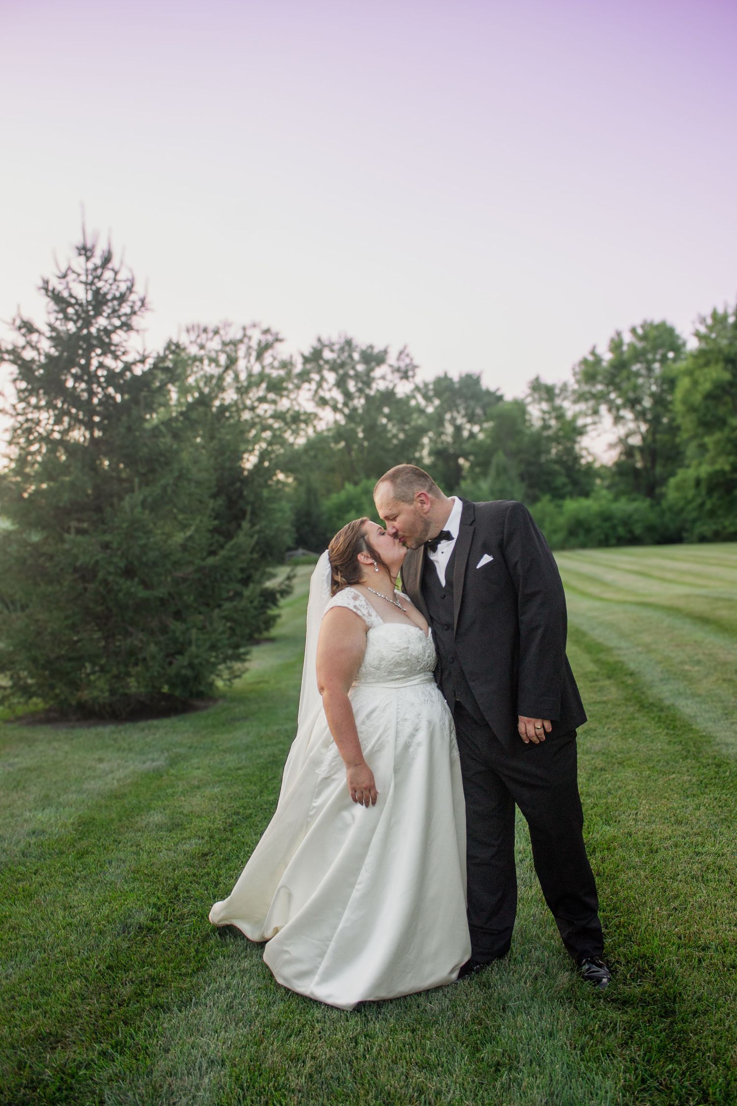 Newlyweds share romantic moment on manicured lawn during sunset wedding photoshoot.