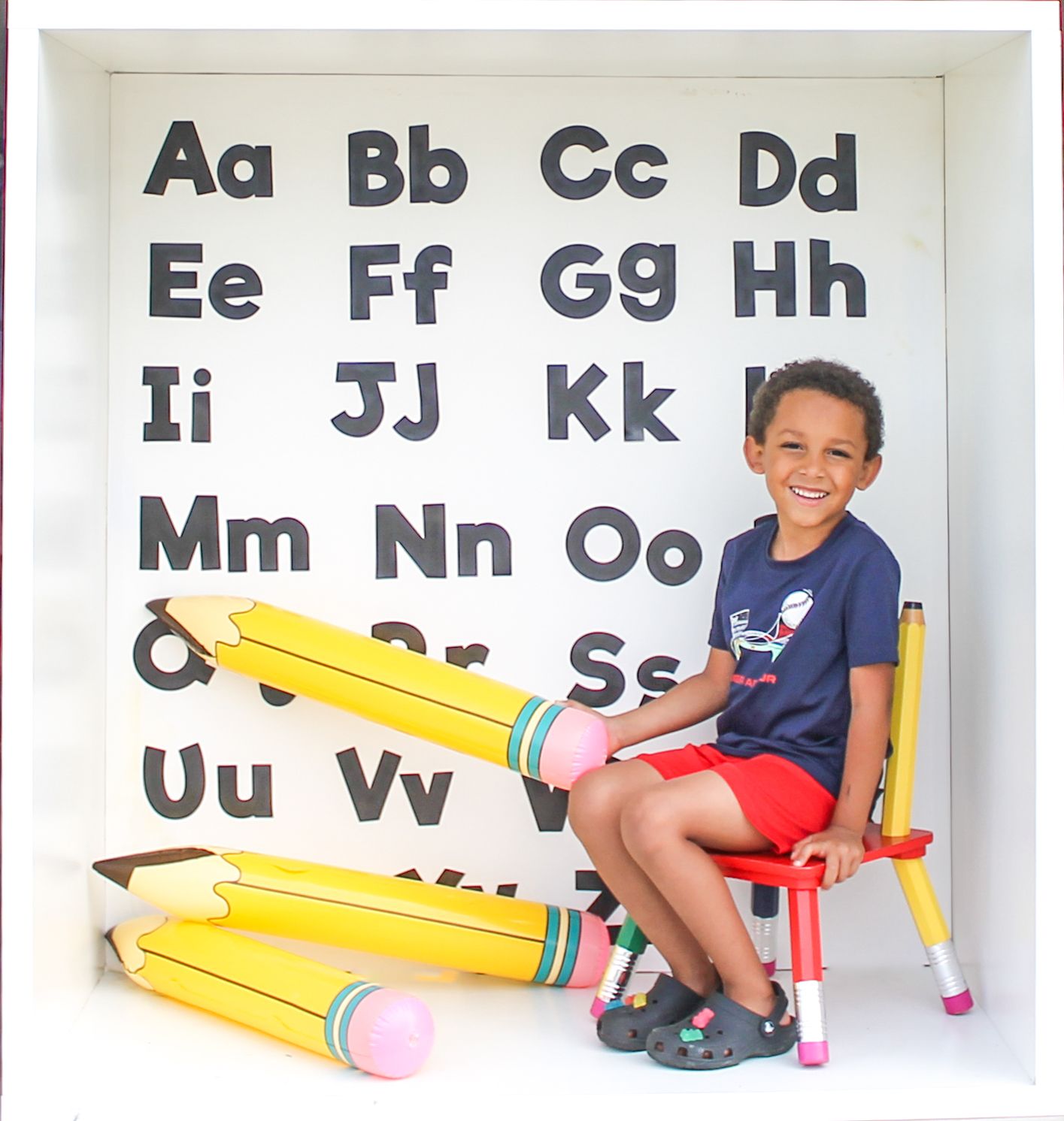 Giant decorative yellow pencils displayed against white wall with alphabet letters.